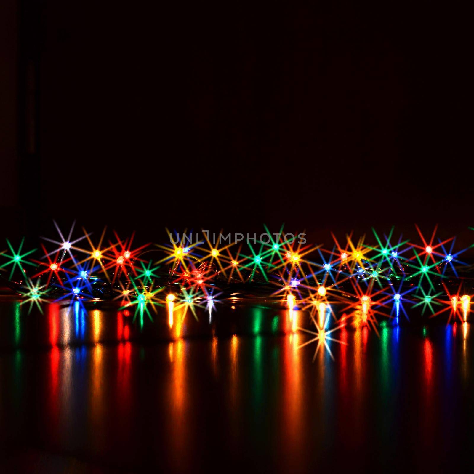 Christmas lights on black background with copy space. Colored reflecting surface.