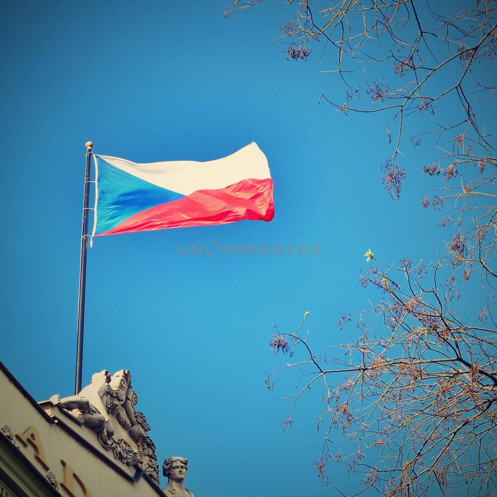 The flag of the Czech Republic on a building with blue sky and the sun in the background. by Montypeter