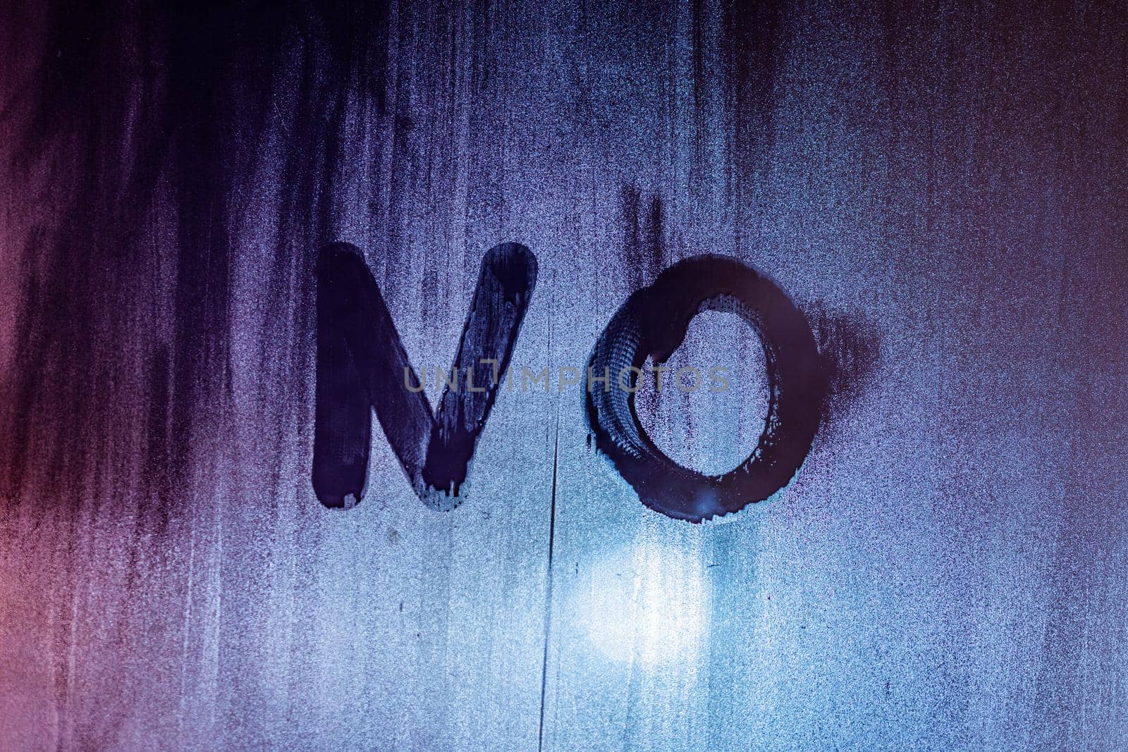 the word no handwritten on night wet window glass surface in blue colors
