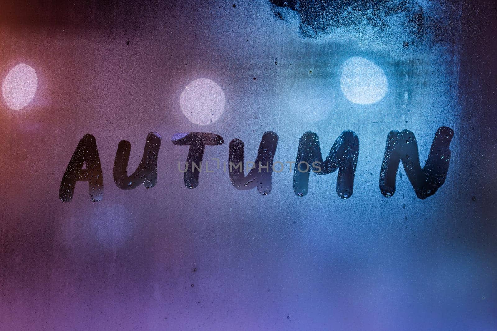 the word autumn handwritten on night wet window glass surface.