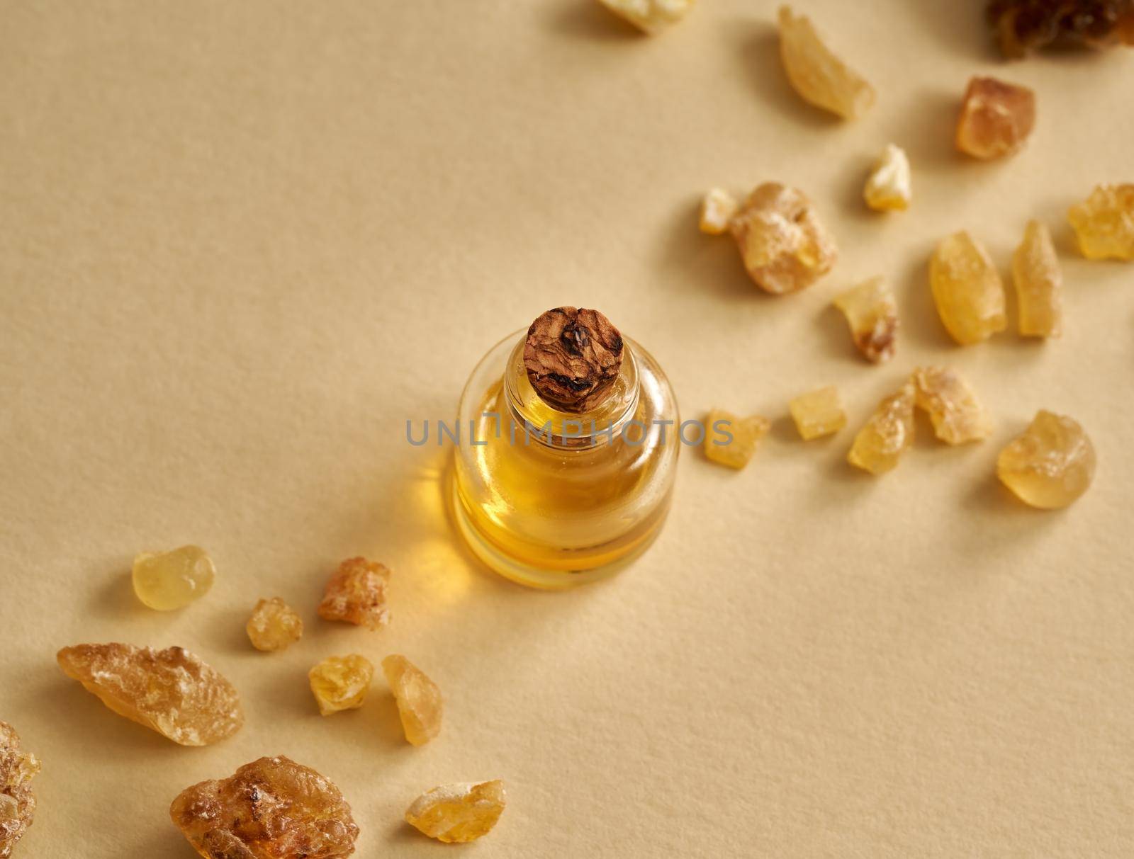 A bottle of essential oil with frankincense resin on pastel yellow background