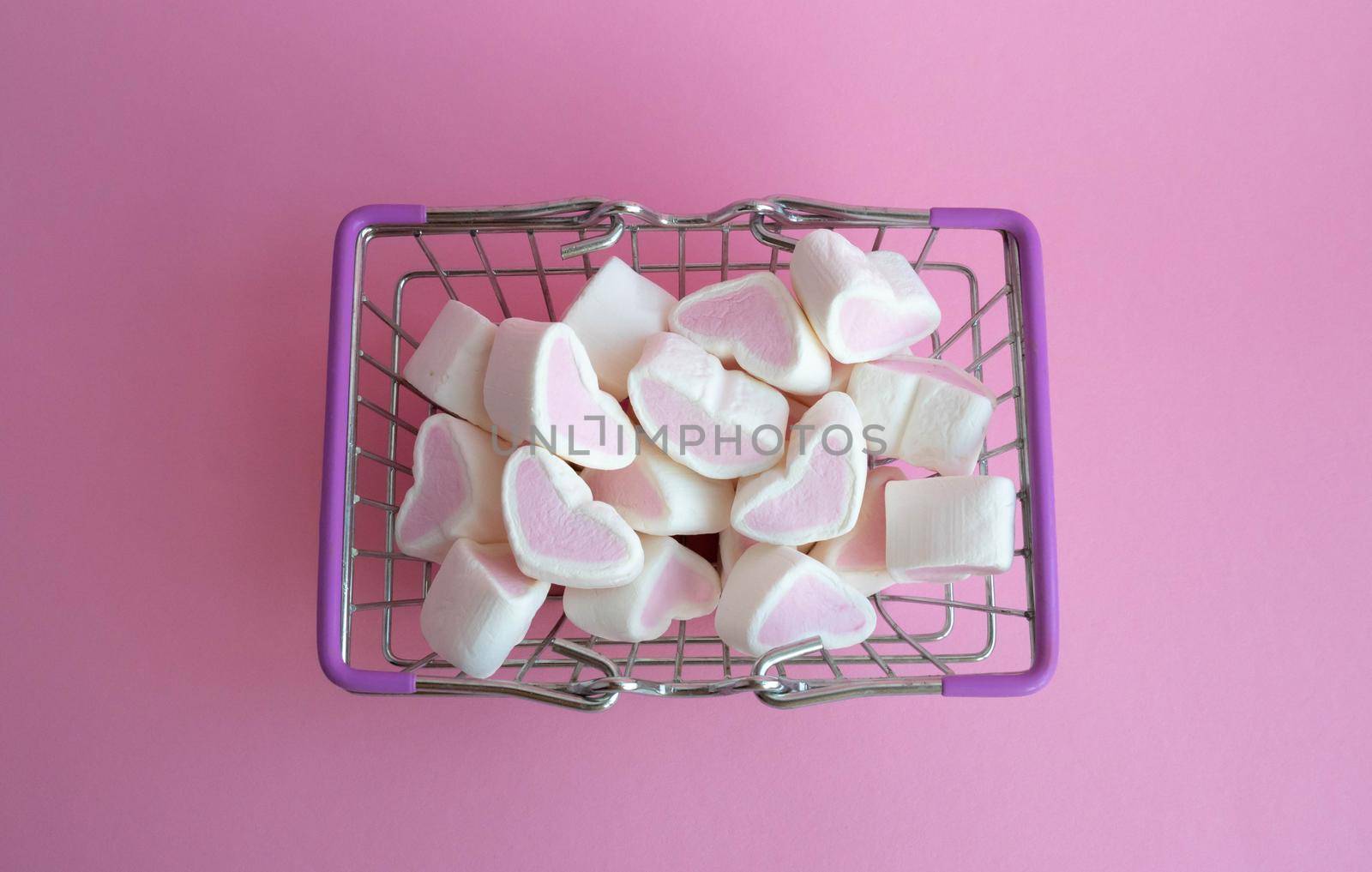 Valentine's Day, top view. Marshmallows pink hearts spilled out of a toy basket on a pink background, copying the space, the concept of love. The concept of buying love