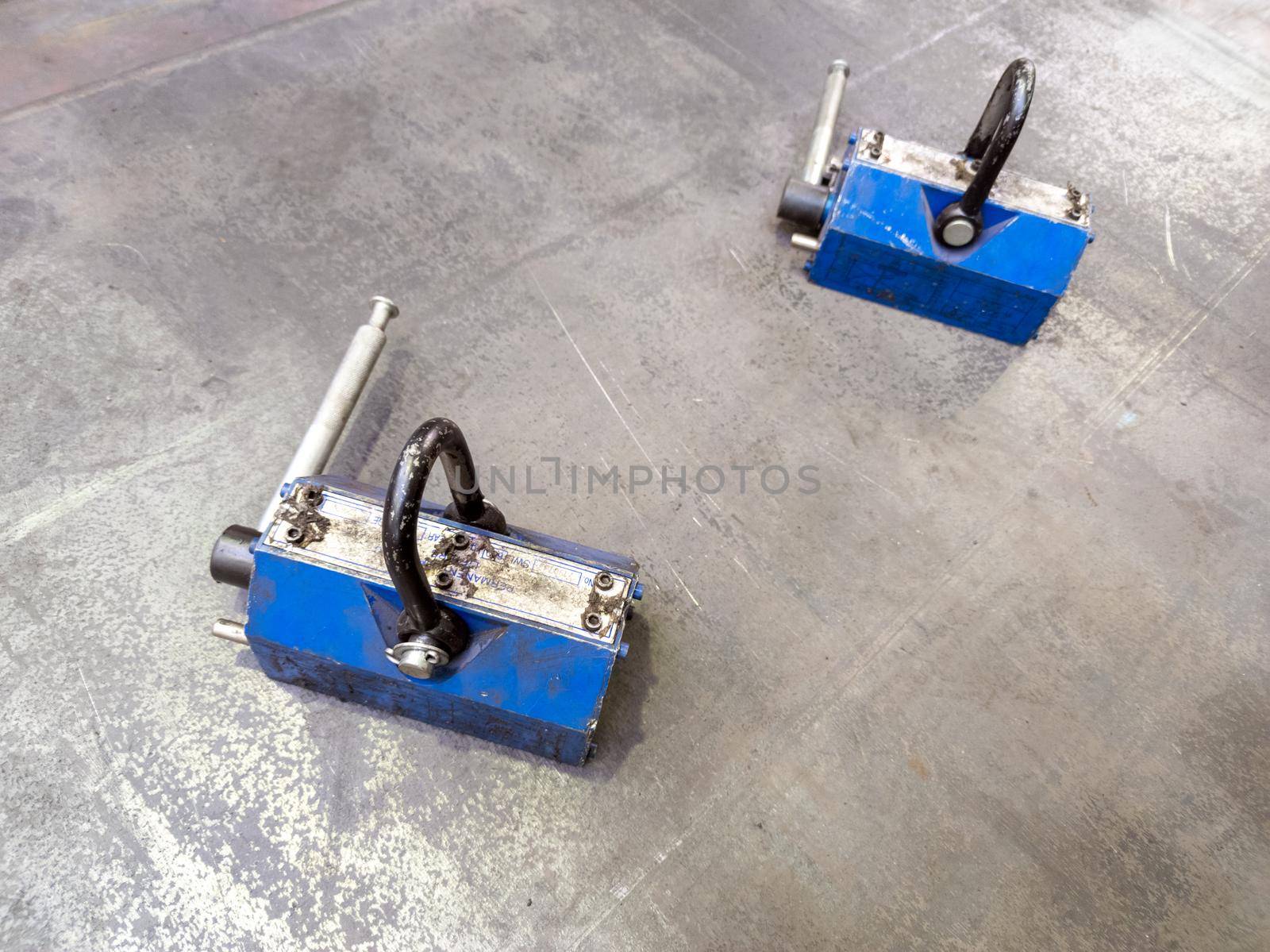 Pair of blue 600 kg industrial lifting magnets on flat sheet metal surface. Workshop handling equipment.
