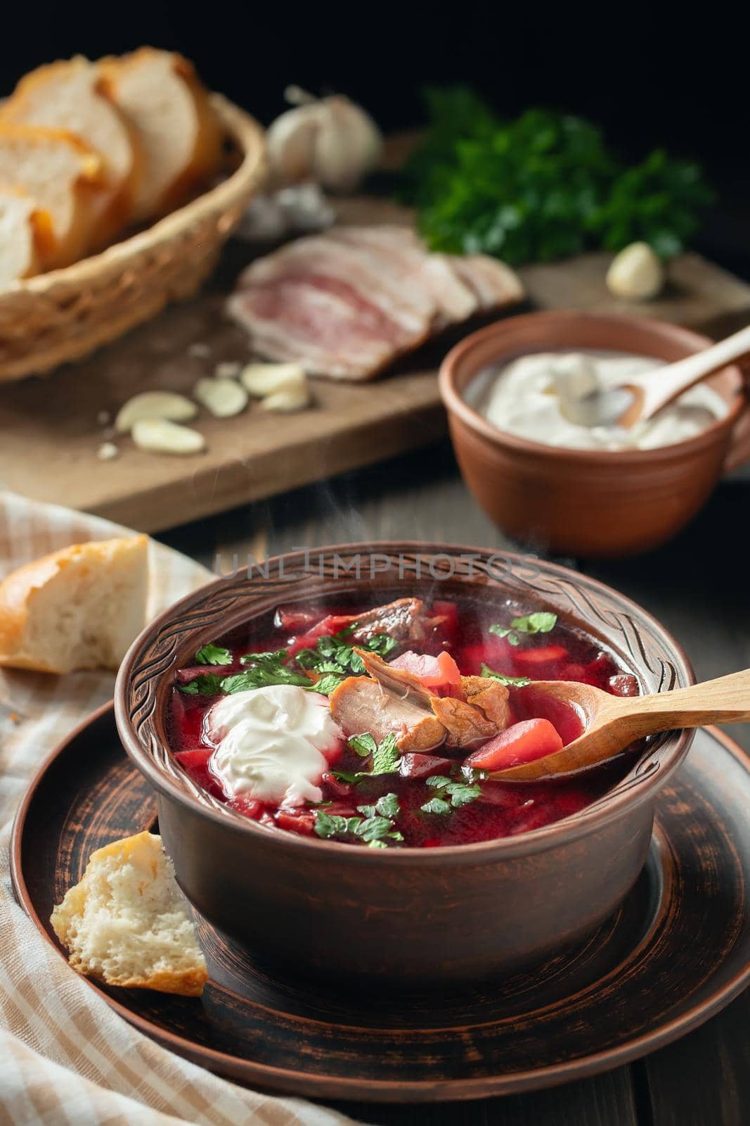 Freshly cooked borscht - traditional dish of Russian and Ukrainian cuisine in earthenware dishes with bacon, sour cream and garlic, vertical image.