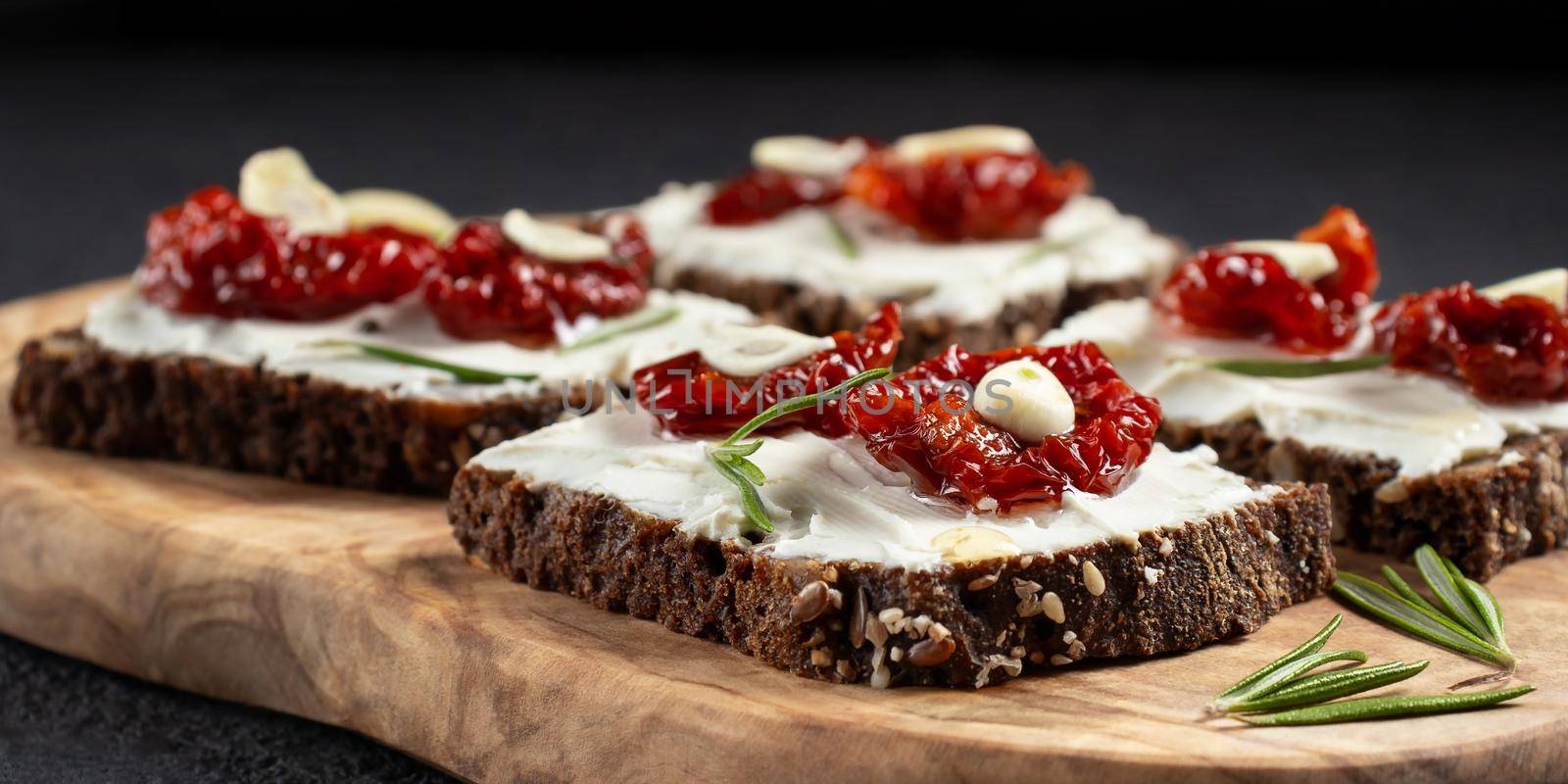 Homemade multigrain bread sandwiches with cream cheese and sun-dried tomatoes on a wooden platter. Healthy eating concept.