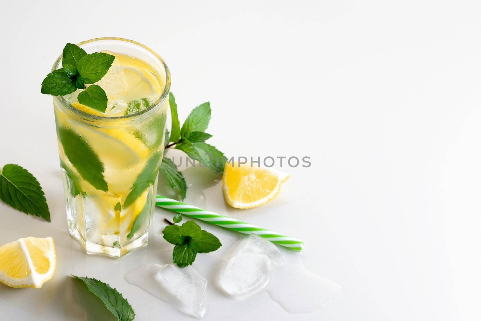 Fresh homemade cocktail with lemon, mint and ice on a white table, copy space by galsand