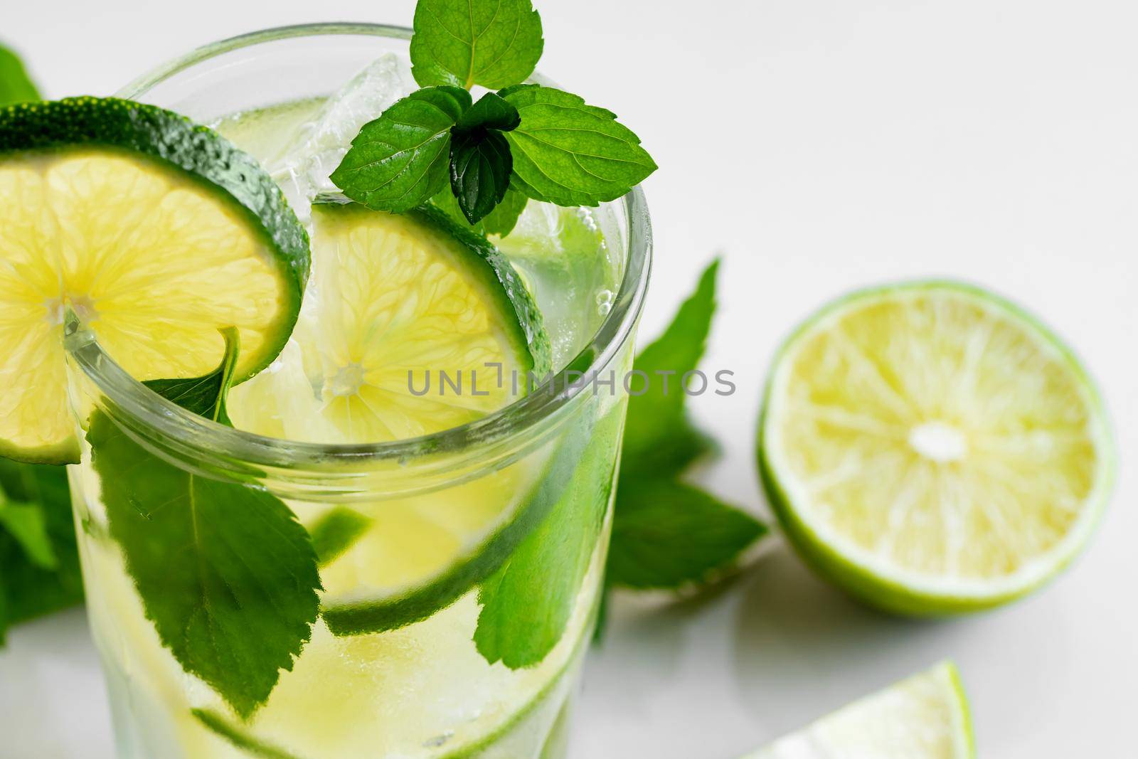 Fresh homemade cocktail with lime, mint and ice on a white table, close up.