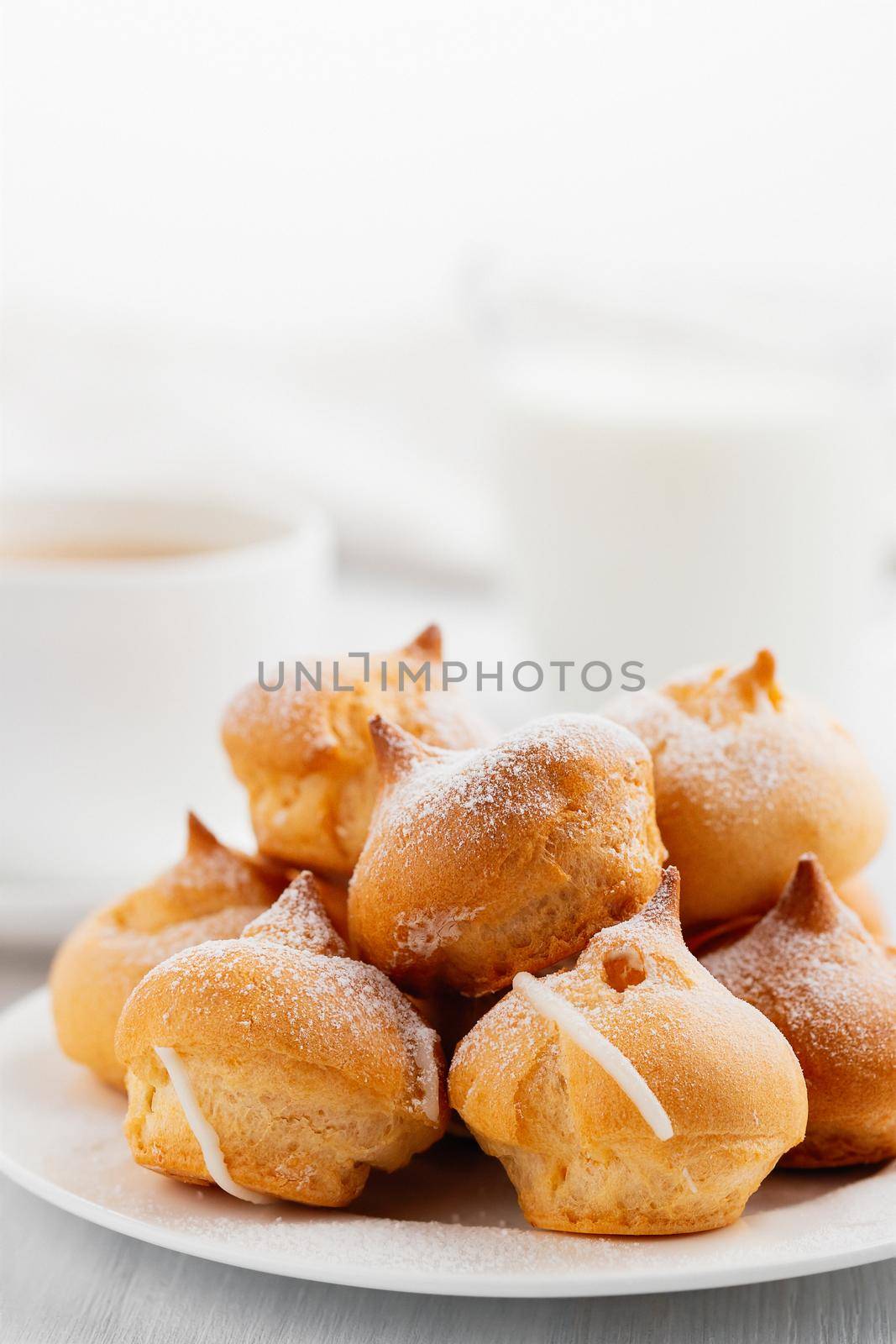 Morning coffee with cakes. Profiteroles, coffee, cream on a white wooden table. Vertical image.