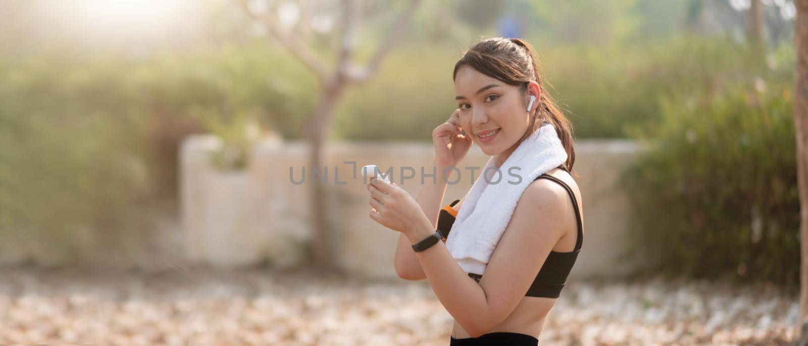 Photo of a beautiful asian young fitness woman running outdoors listening music with earphones by nateemee