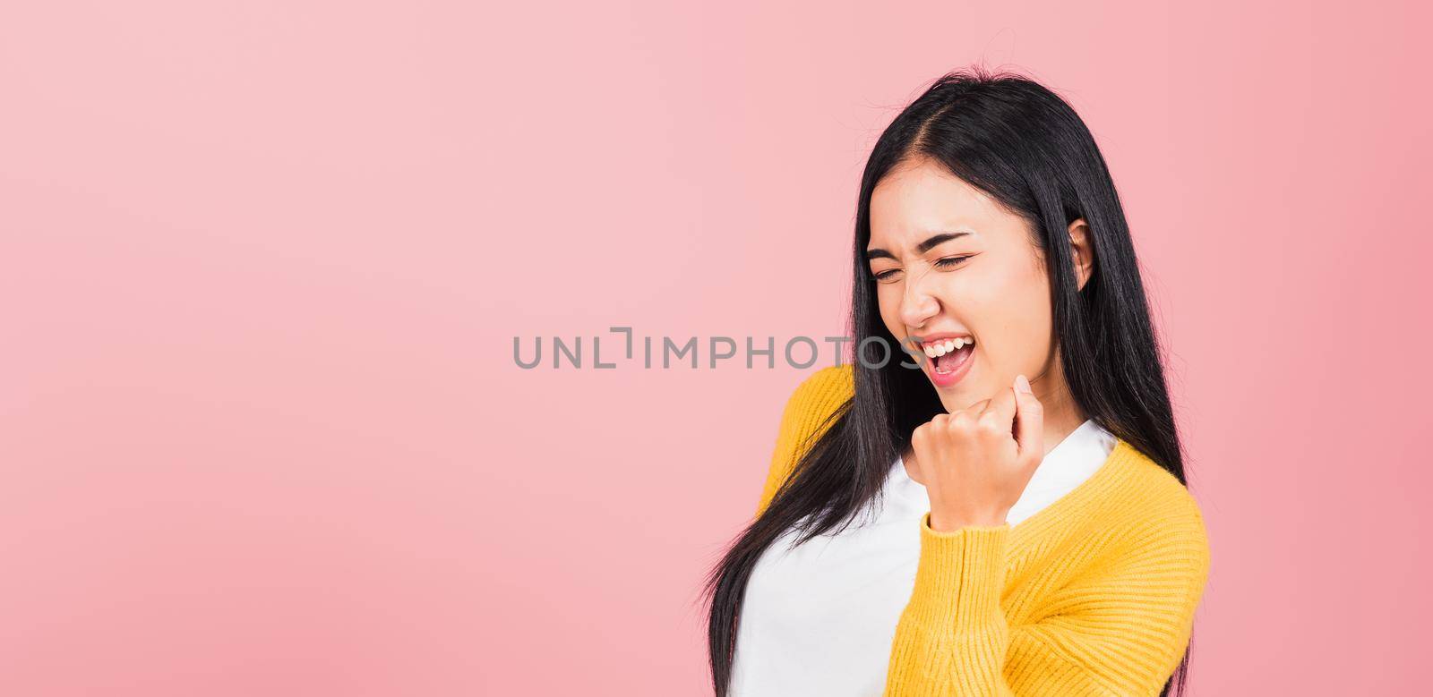 Happy Asian portrait beautiful cute young woman stand makes raised fists up celebrating her winning success gesture, studio shot isolated pink background, Thai female excited say yes! with copy space