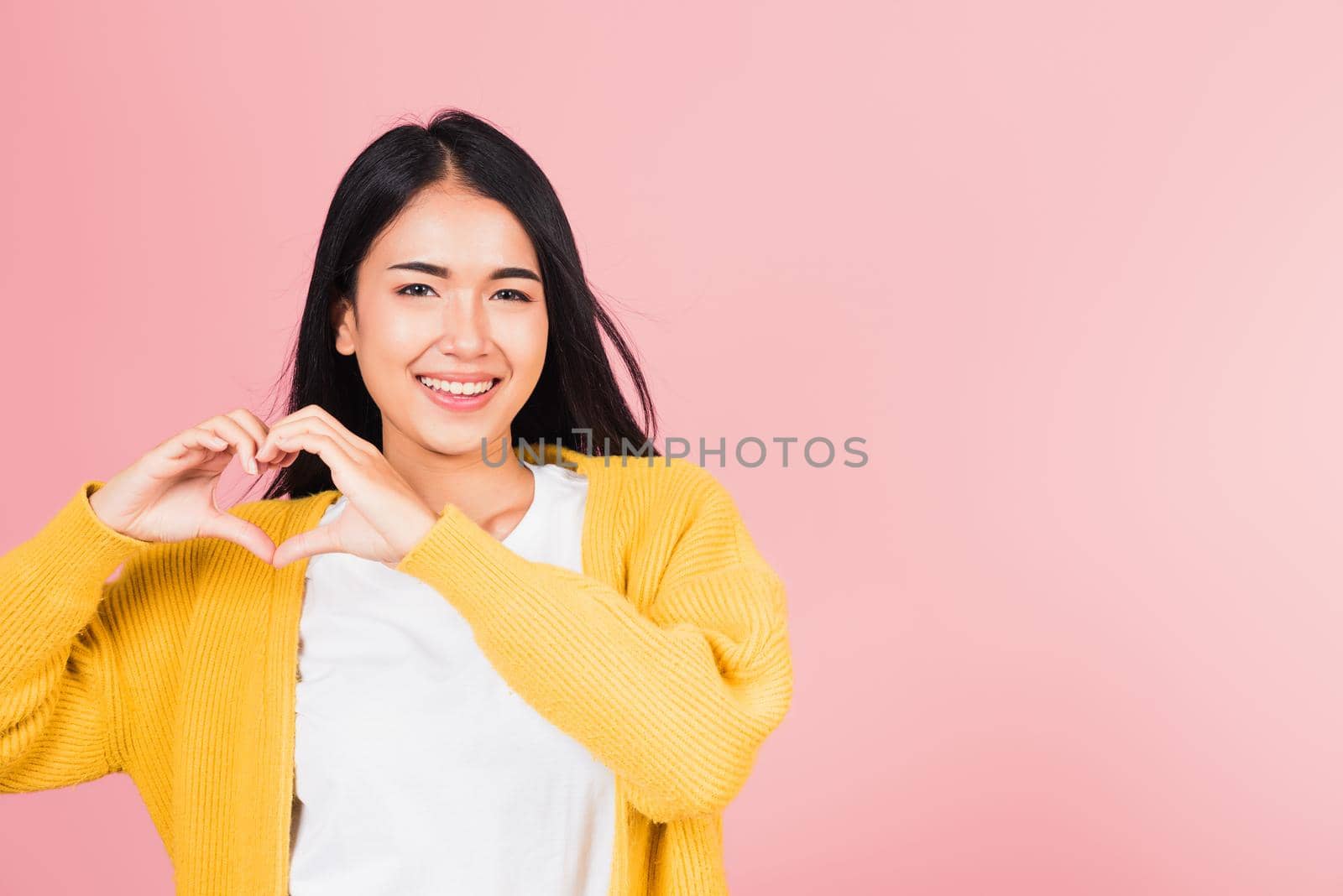 Happy Asian portrait beautiful cute young woman smile make finger heart gesture figure symbol shape sign with two hands sending love to her lover looking camera, studio shot isolated pink background