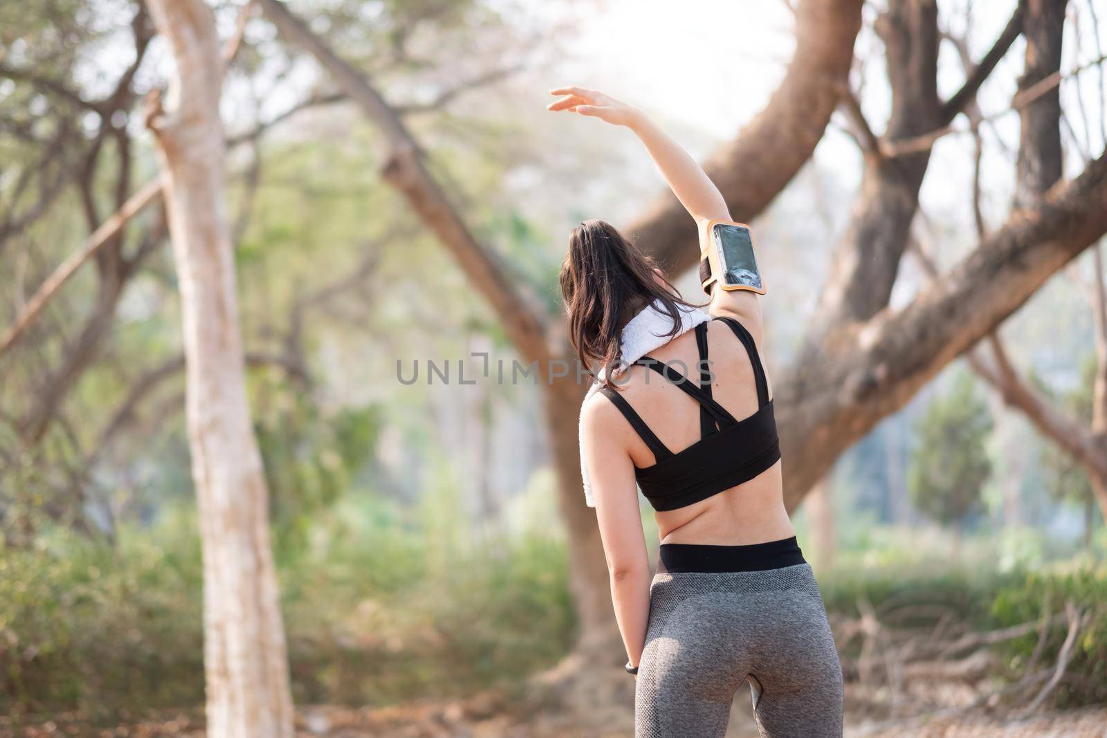 Athletic woman warming up before a workout standing facing the early morning rising sun at park by nateemee