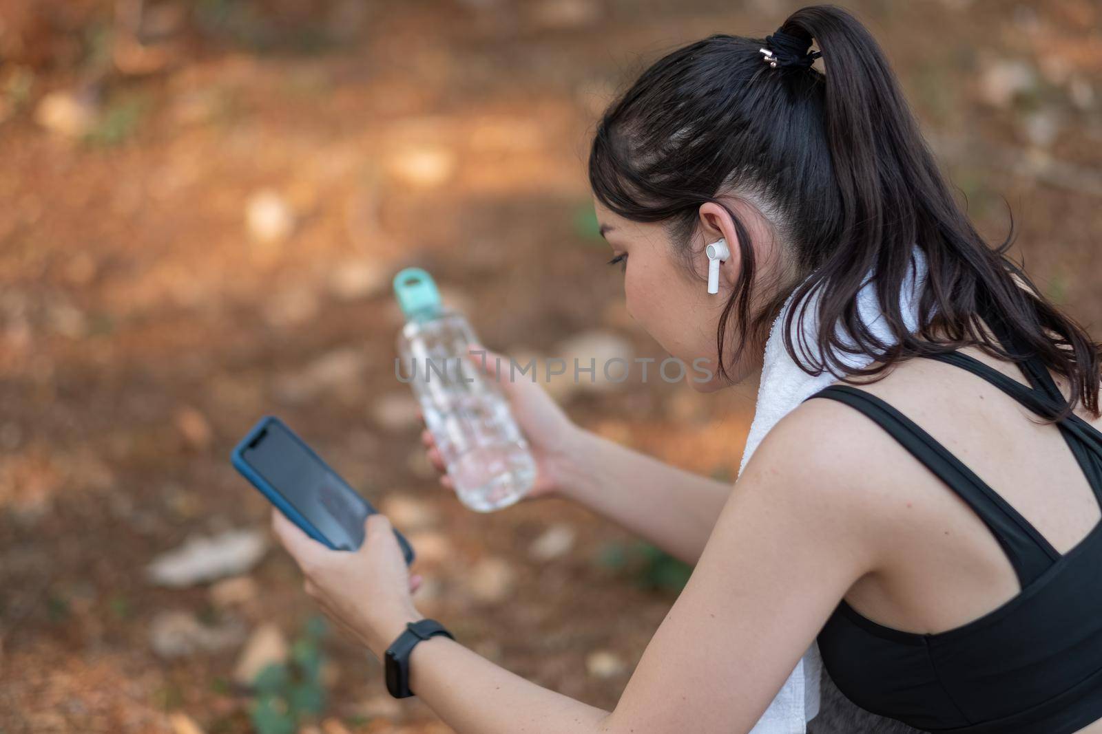 Tired fitness woman sweating taking a break listening to music on phone after difficult training by nateemee