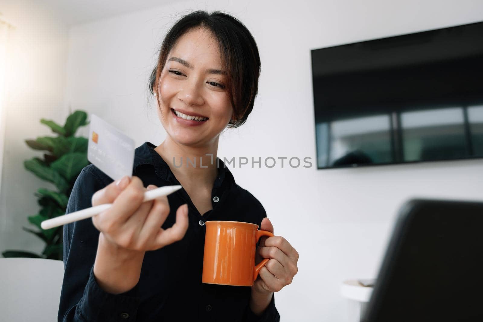 Happy woman holding credit card while using laptop computer for online shopping at home.