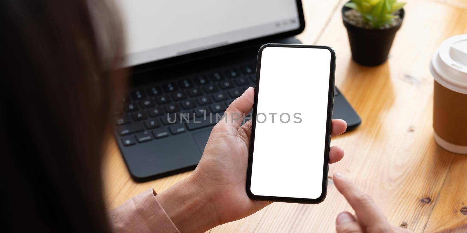 Top view Woman sitting on work desk and holding blank screen mock up mobile phone