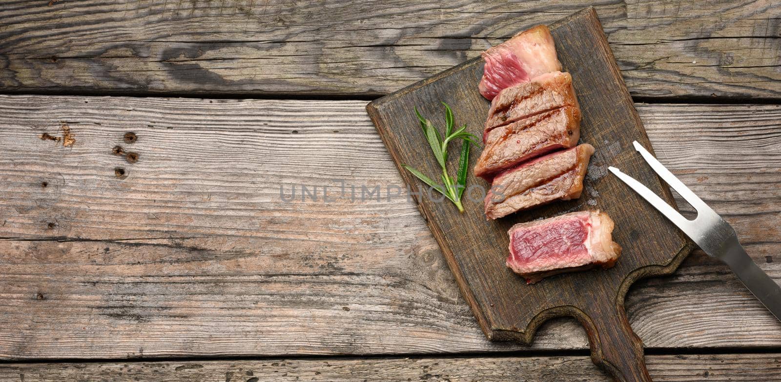 sliced fried beef steak New York striploin on a wooden cutting board, degree of doneness rare, copy space