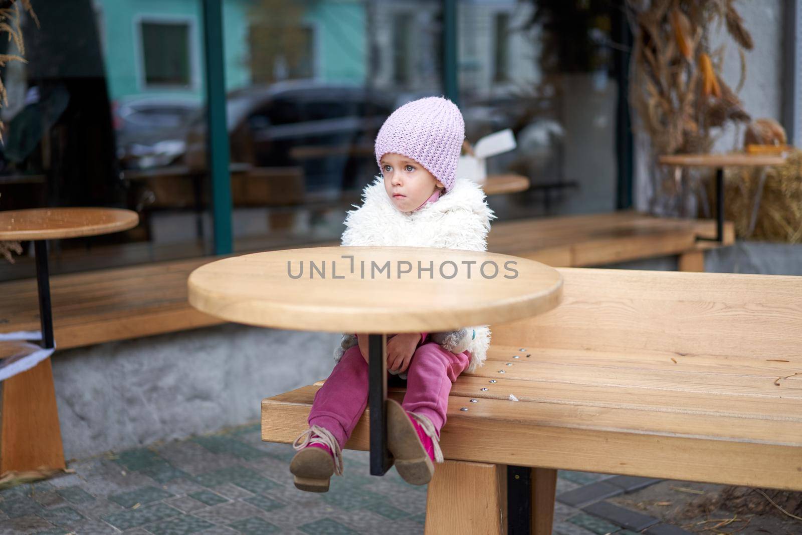 Unhappy little girl sitting outdoor cafe at table autumn season Caucasian female child losy in city sitting sad Lonely