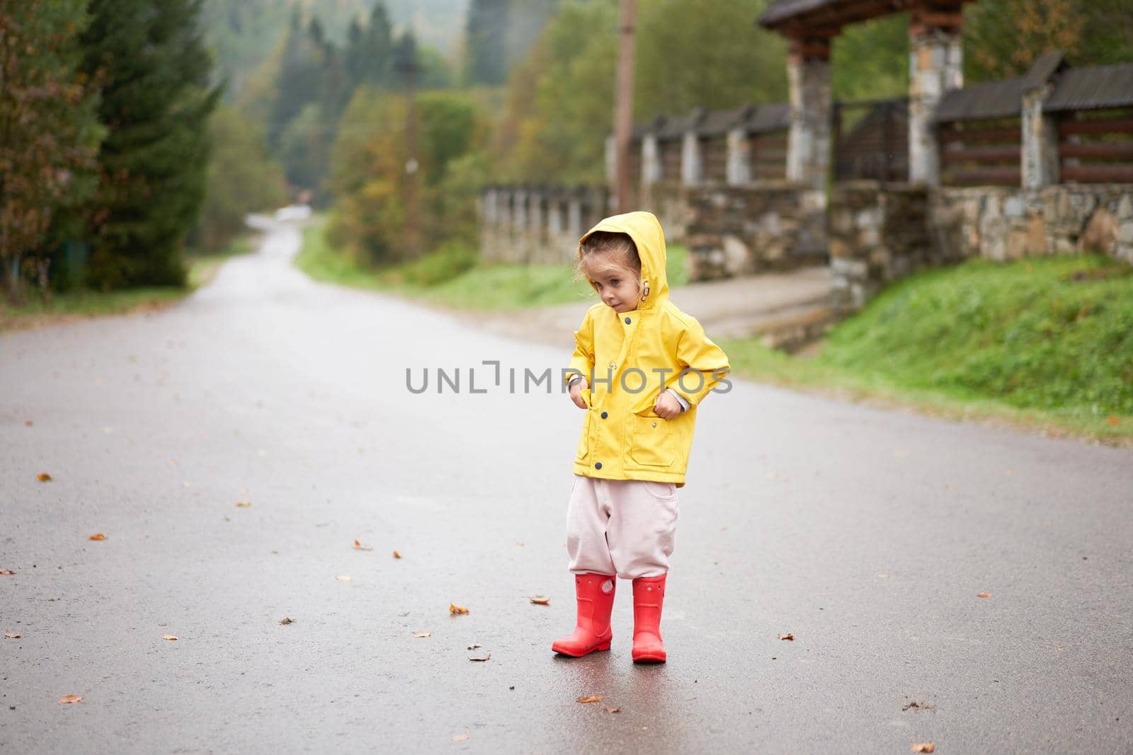 Playful girl wearing yellow raincoat while jumping in puddle during rainfall by andreonegin