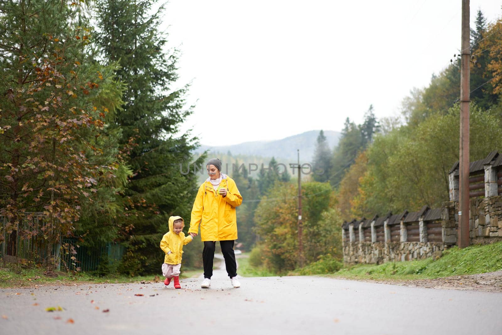 Rainy day Mother and little daughter walking after rain dressed yellow raincoat by andreonegin