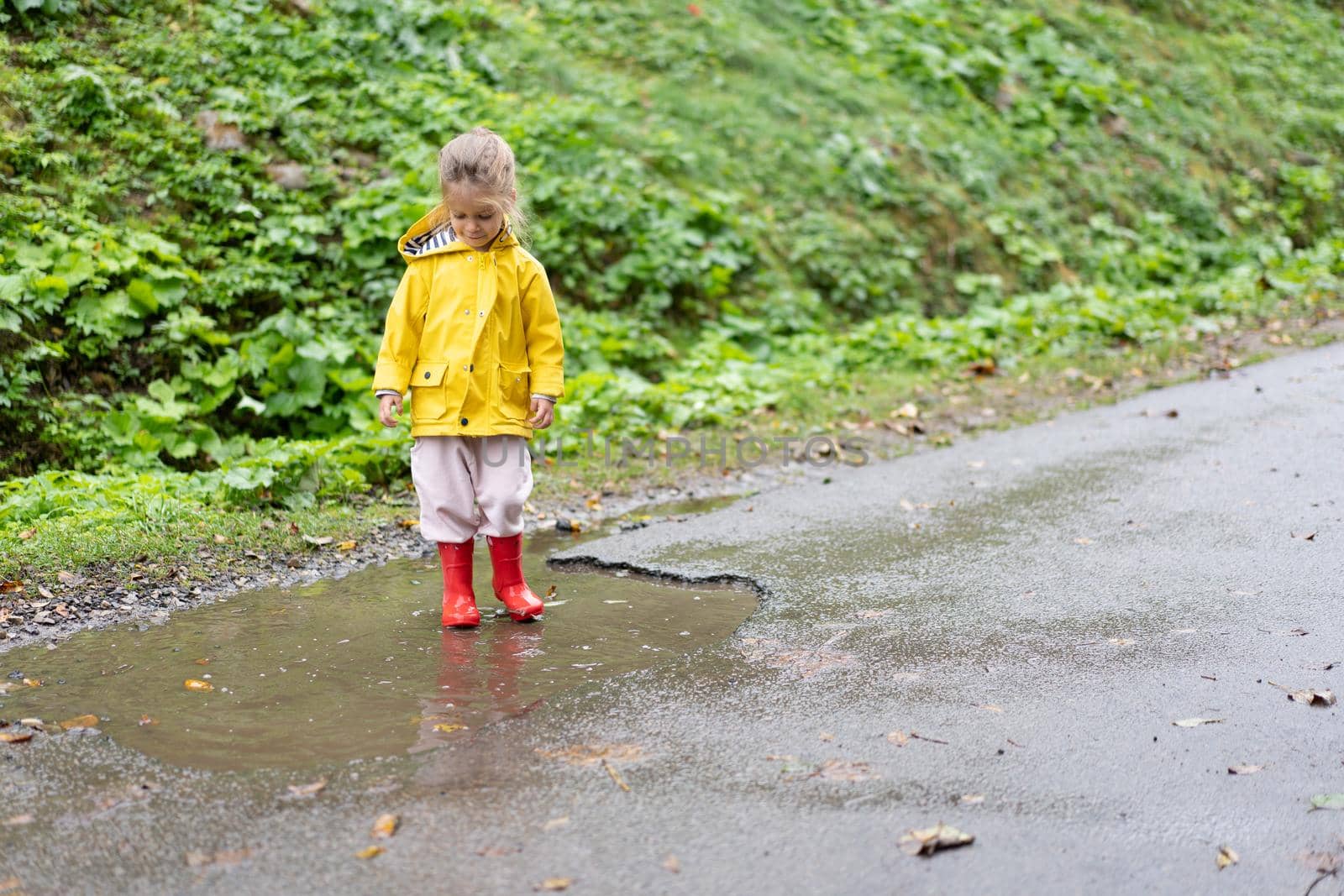 Playful girl wearing yellow raincoat while jumping in puddle during rainfall Happy childhood