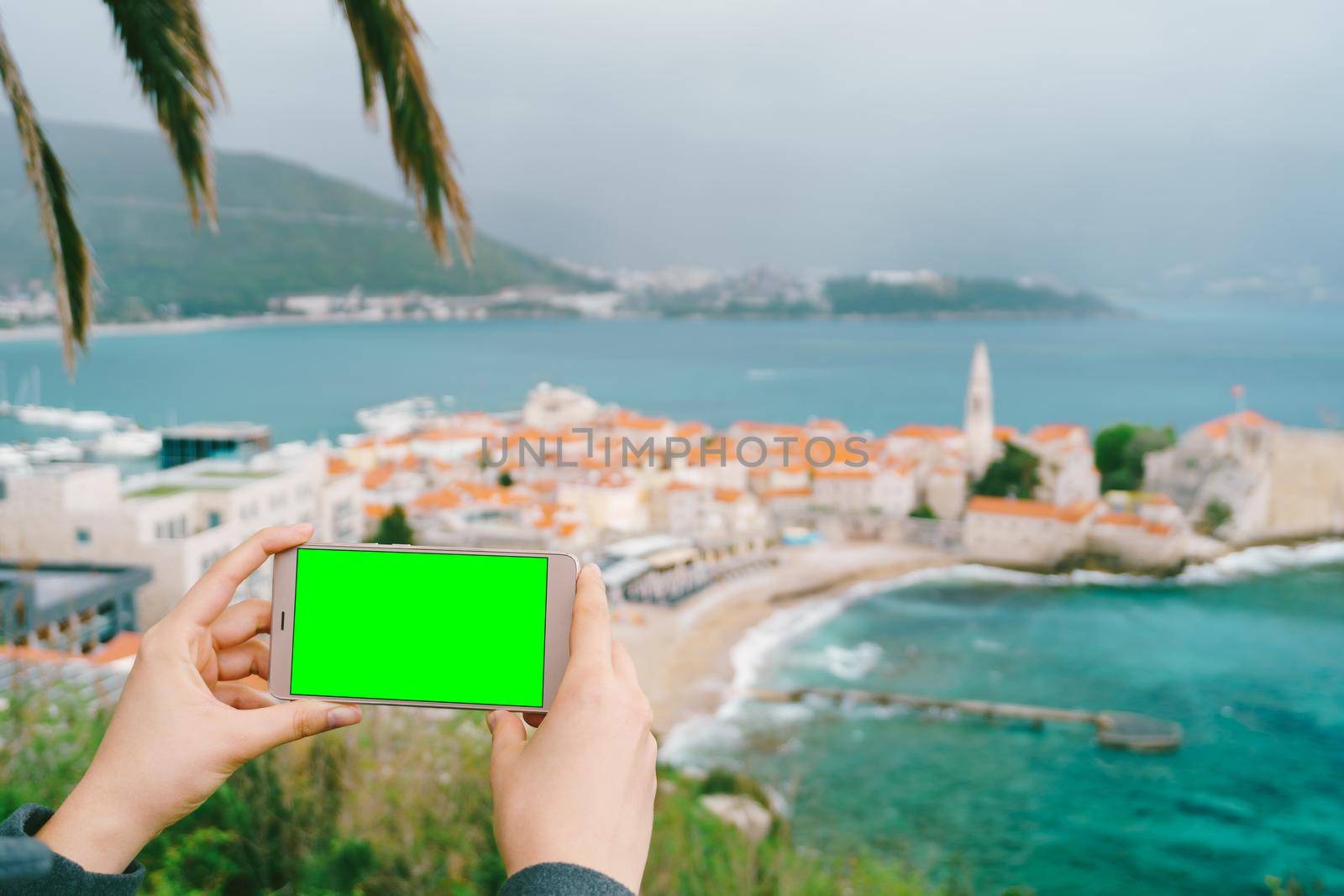 Smartphone in hands with a blank screen on the background of Budva. High quality photo
