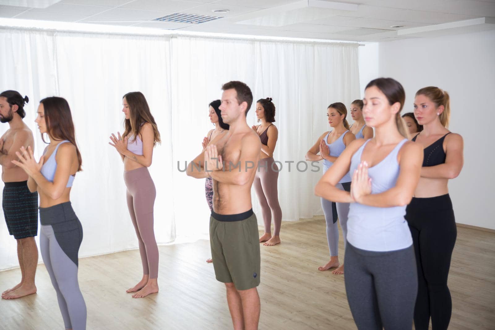 Group of young sporty attractive people in yoga studio, practicing yoga lesson with instructor, standing, stretching and relaxing after workout . Healthy active lifestyle, working out indoors in gym.