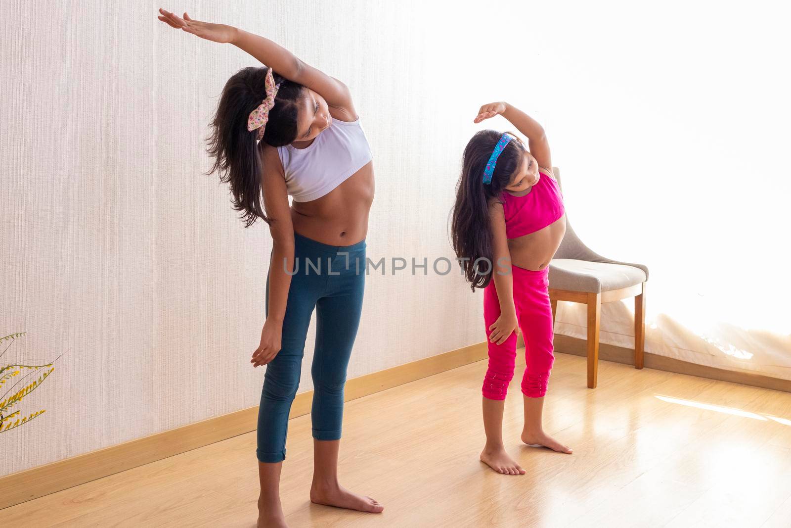 Two little sisters are doing exercise routines in the living room at home
