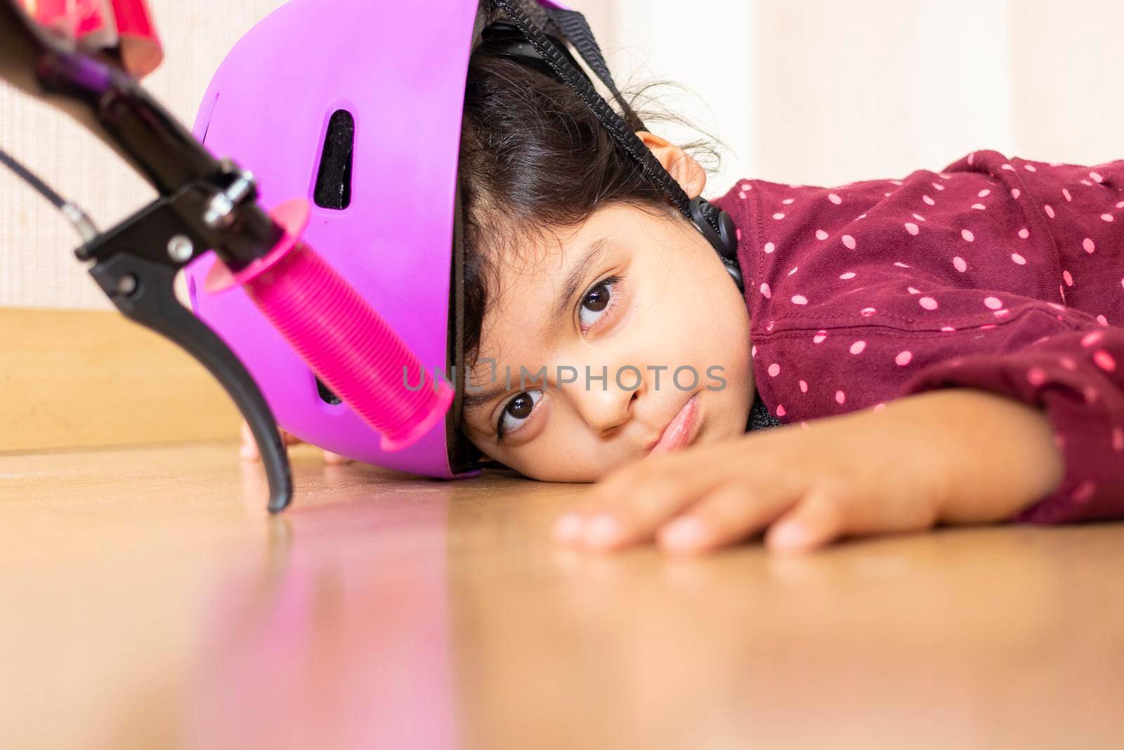 Sad little girl fell to the ground while playing with her bicycle in the house