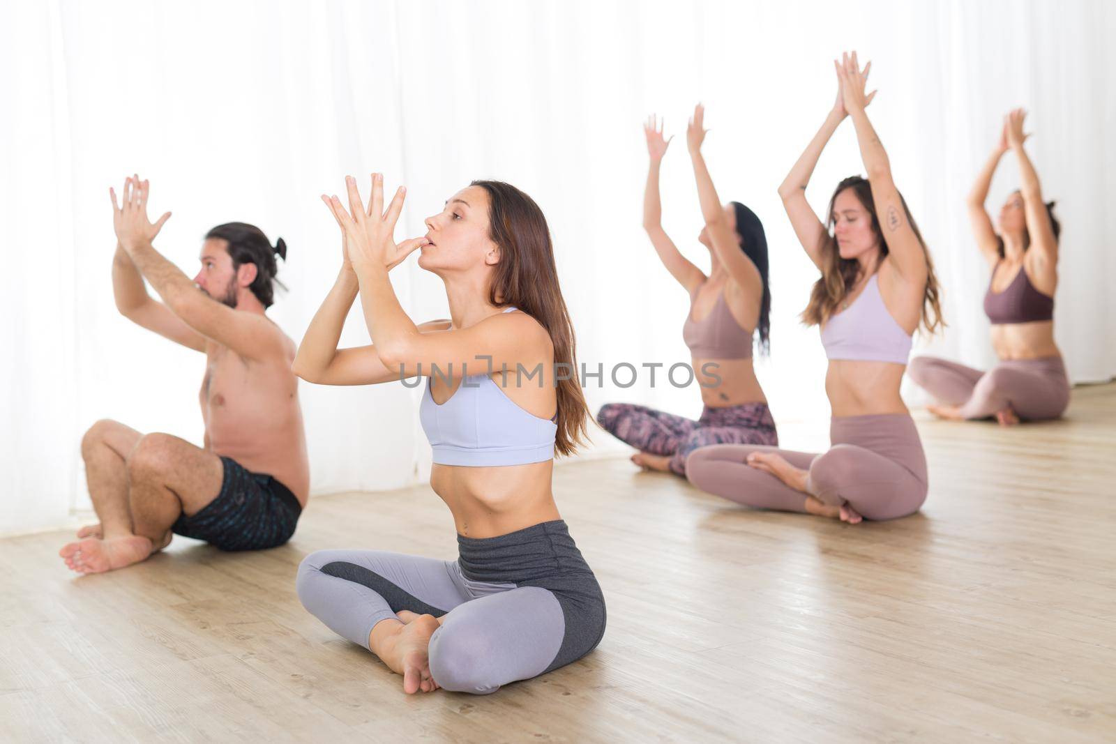 Group of young authentic sporty attractive people in yoga studio, practicing yoga lesson with instructor. Healthy active lifestyle, working out in gym.