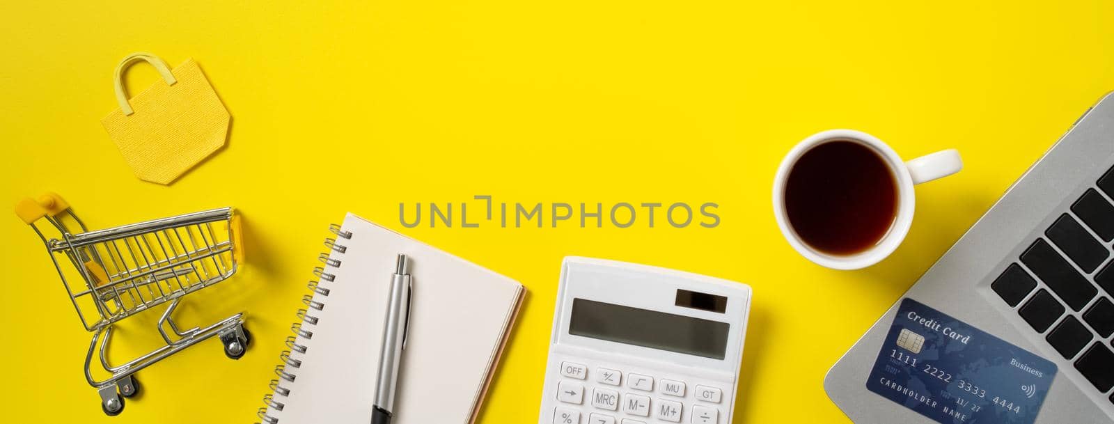 Online shopping concept. Top view of credit card purchase design concept with note, calculator and computer isolated on office yellow table background.