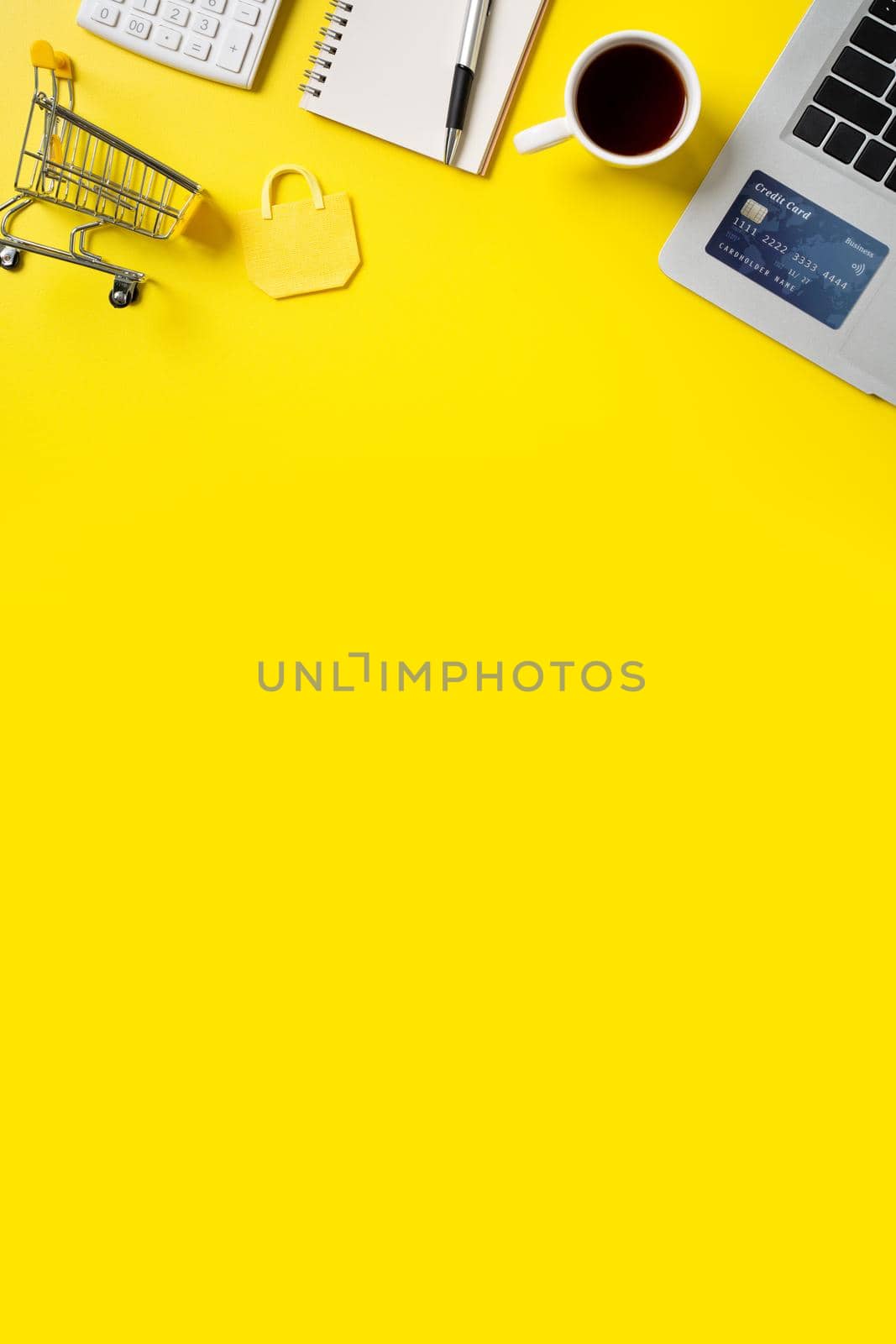 Online shopping concept. Top view of credit card purchase design concept with note, calculator and computer isolated on office yellow table background.