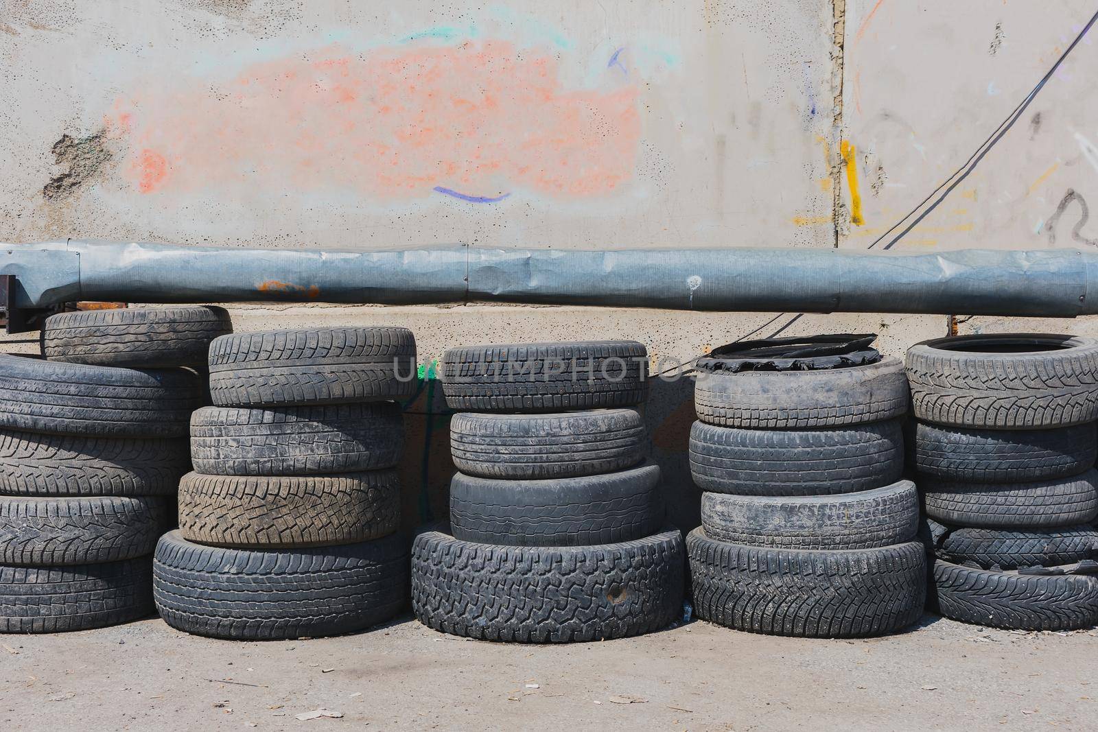 Folded worn car tires near a wall in a junkyard
