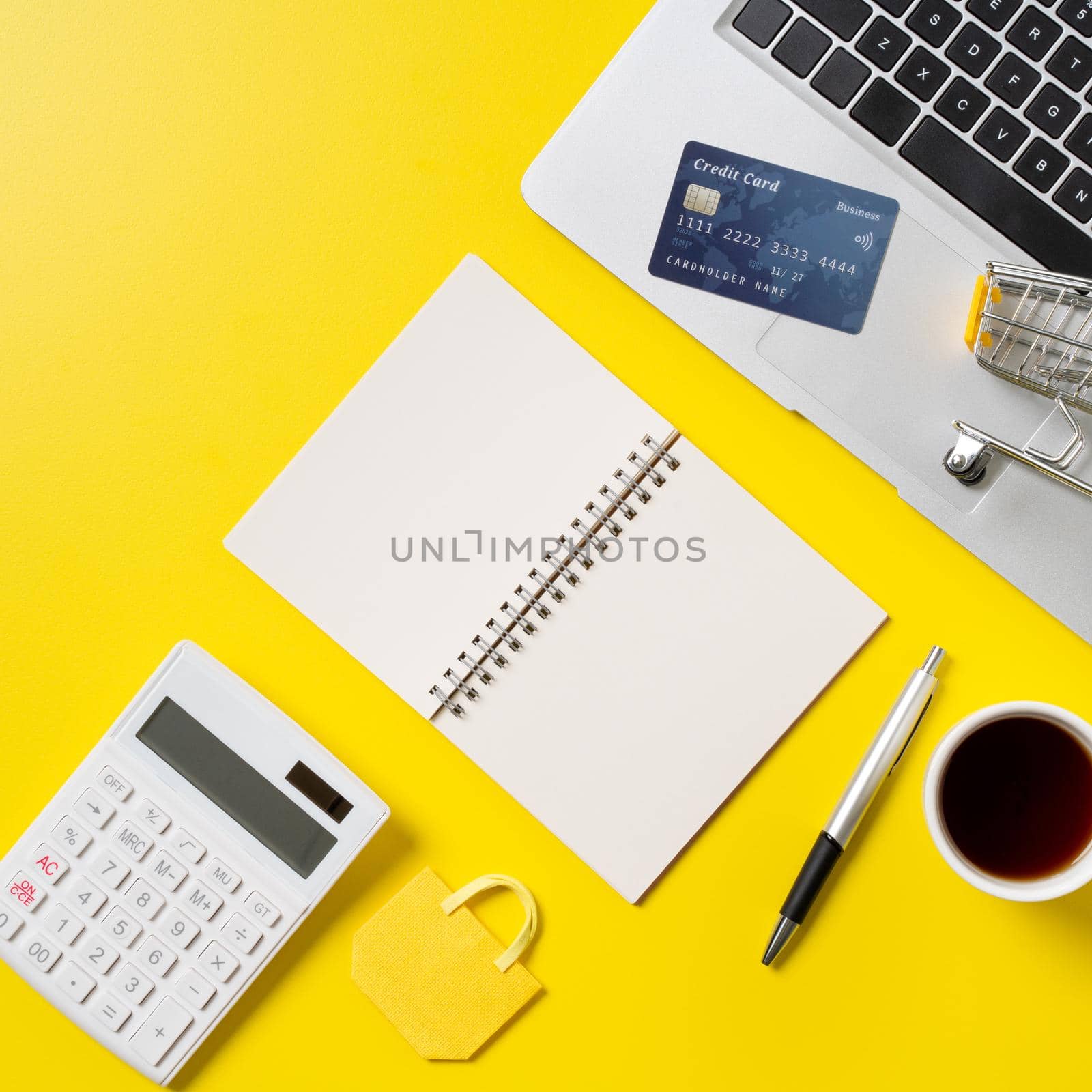 Online shopping concept. Top view of credit card purchase design concept with note, calculator and computer isolated on office yellow table background.