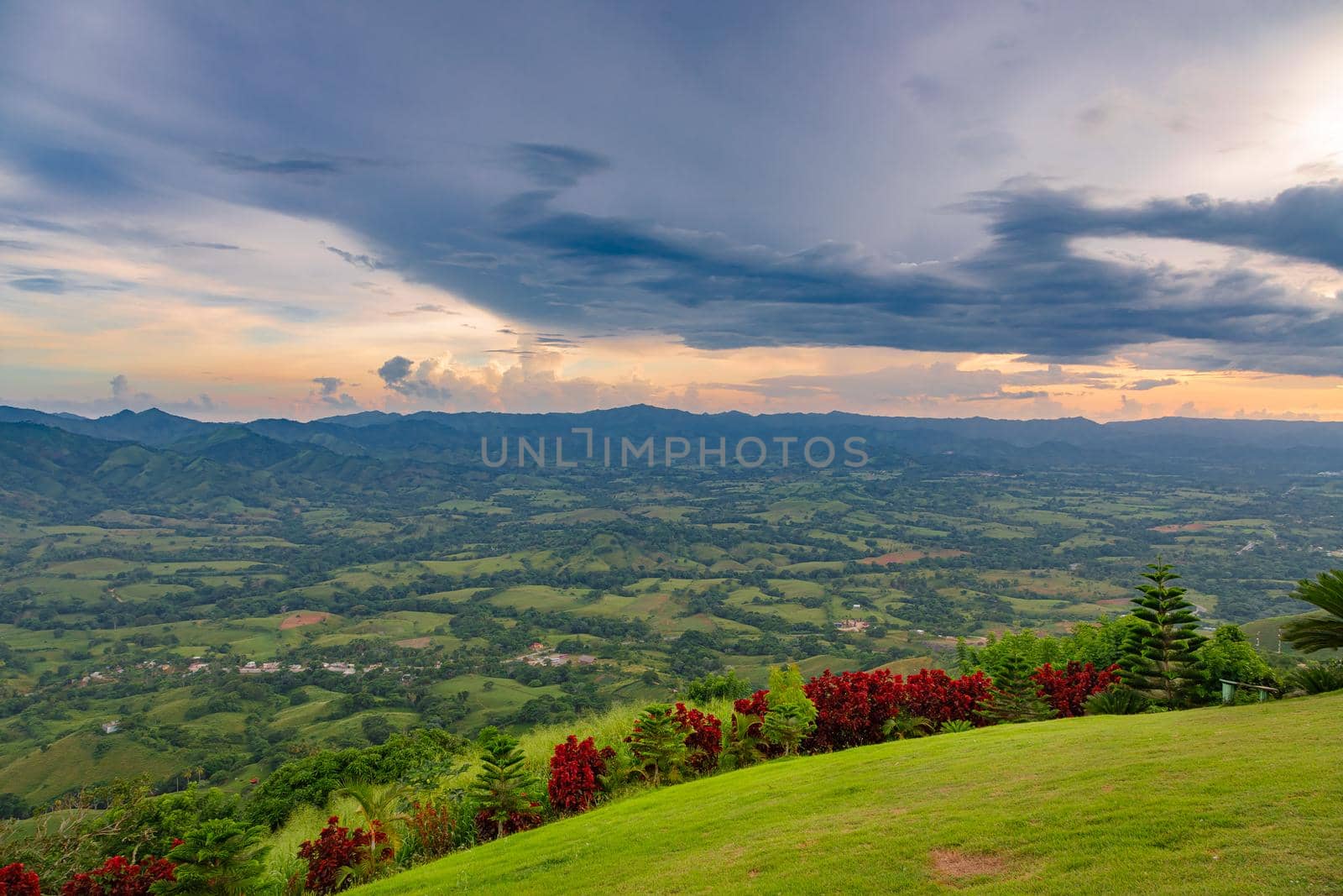 View from a large mountain to a valley with a lake in the Dominican Republic. Setting sun. Around greenery and red bushes
