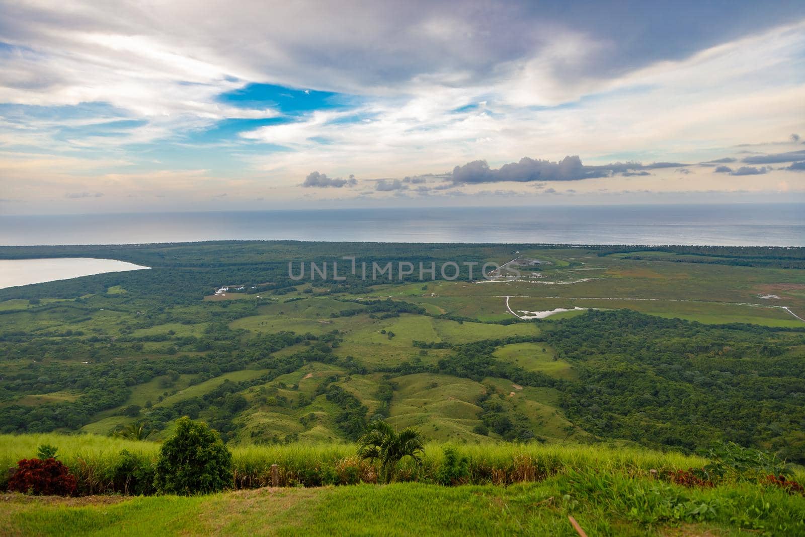 View from a large mountain to a valley with a lake in the Dominican Republic. Setting sun. Around greenery and red bushes