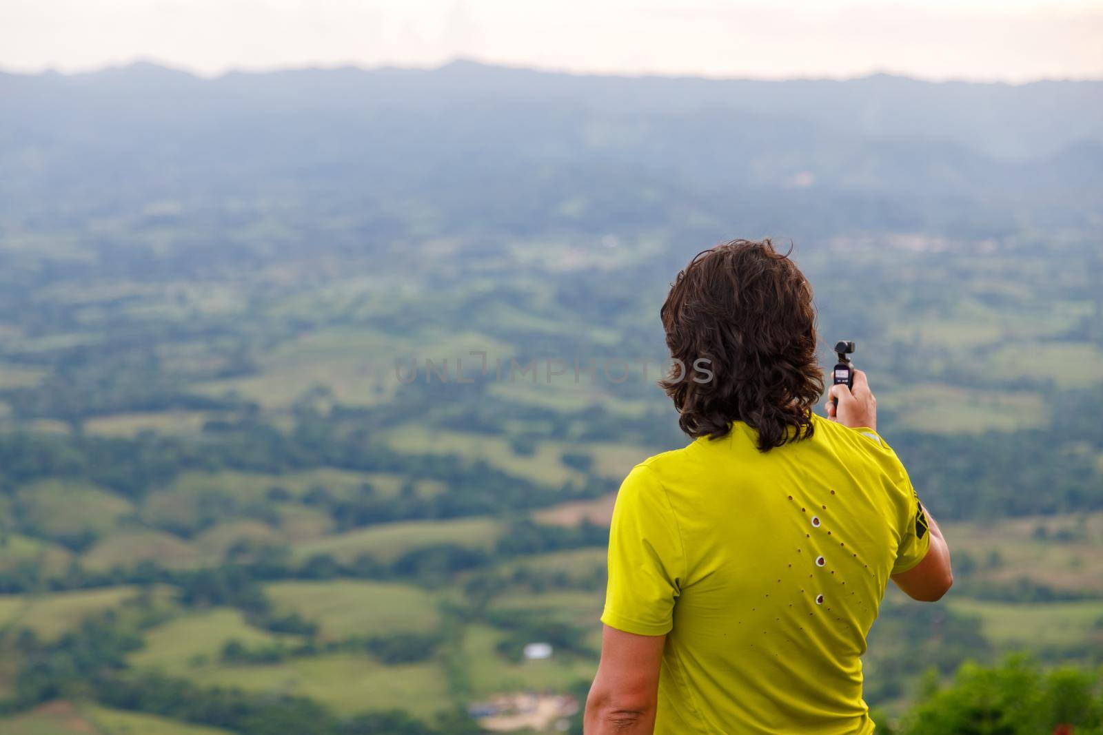 A long-haired man filming a video with a small video camera, a picturesque valley. Dominican Republic on the mountain.