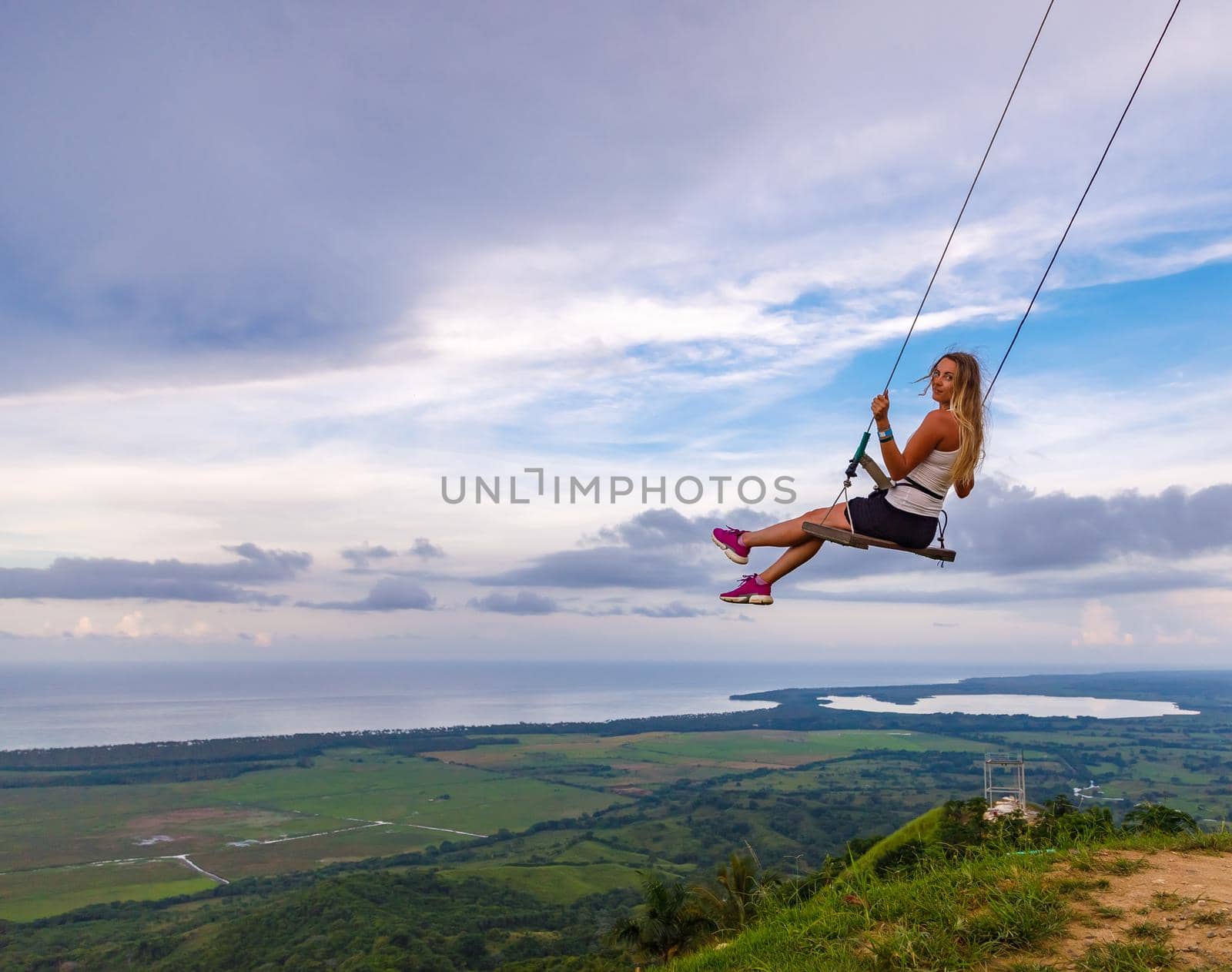 A young girl, blonde, swinging on a swing on a mountain slope in summer. by Yurich32