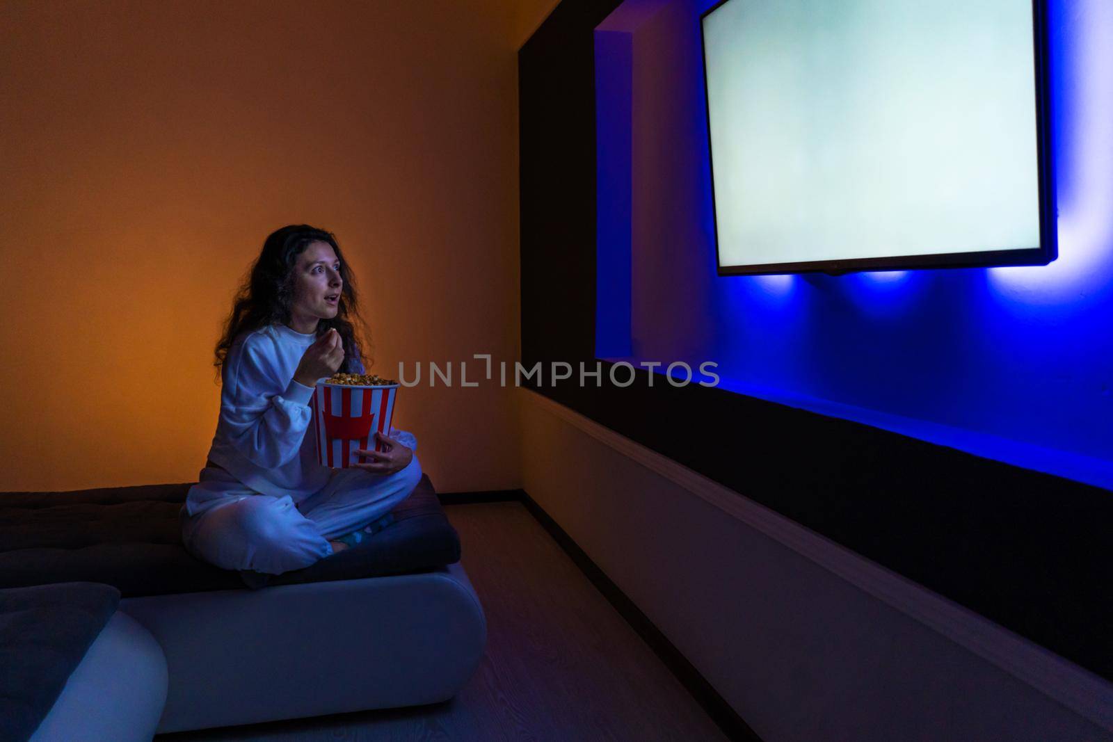 person watches a movie sitting on the couch with a bucket of popcorn.