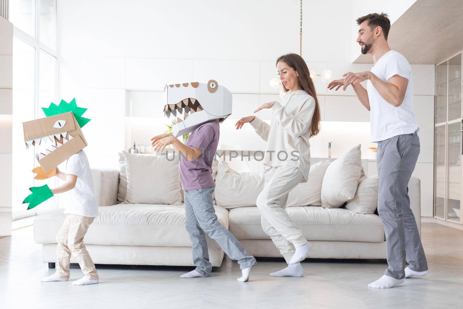 Happy family of parents and two children playing dinosaurs at home, children wearing handmade costume mask of cardboard