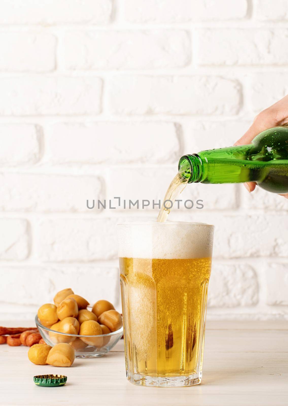 Jet of beer out of the bottle is poured into a beer glass, causing a lot of bubbles and foam, white brick wall background