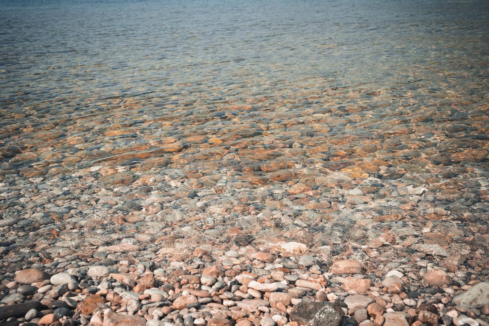 Sea pebbles and stones underwater. Textural seabed through clear transparent blue water. Natural background.