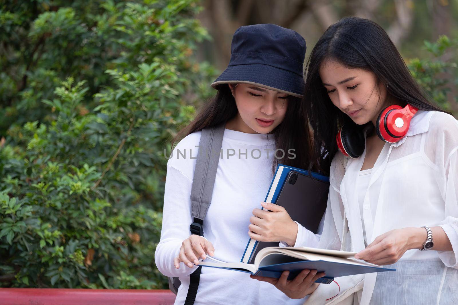 Group of attractive young people reading a book and tablet, school folders reading book at high school university campus college knowledge center for learning in summer outdoor by nateemee