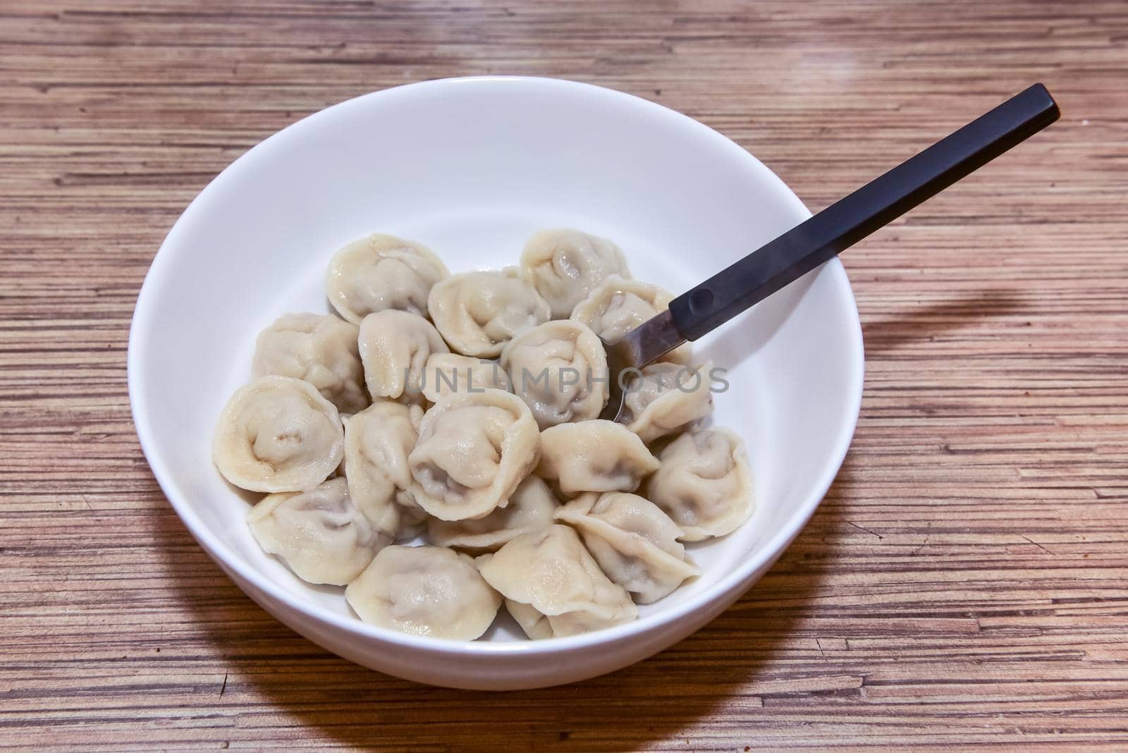 plate with homemade Russian dumplings on a wooden table and a spoon next to it.