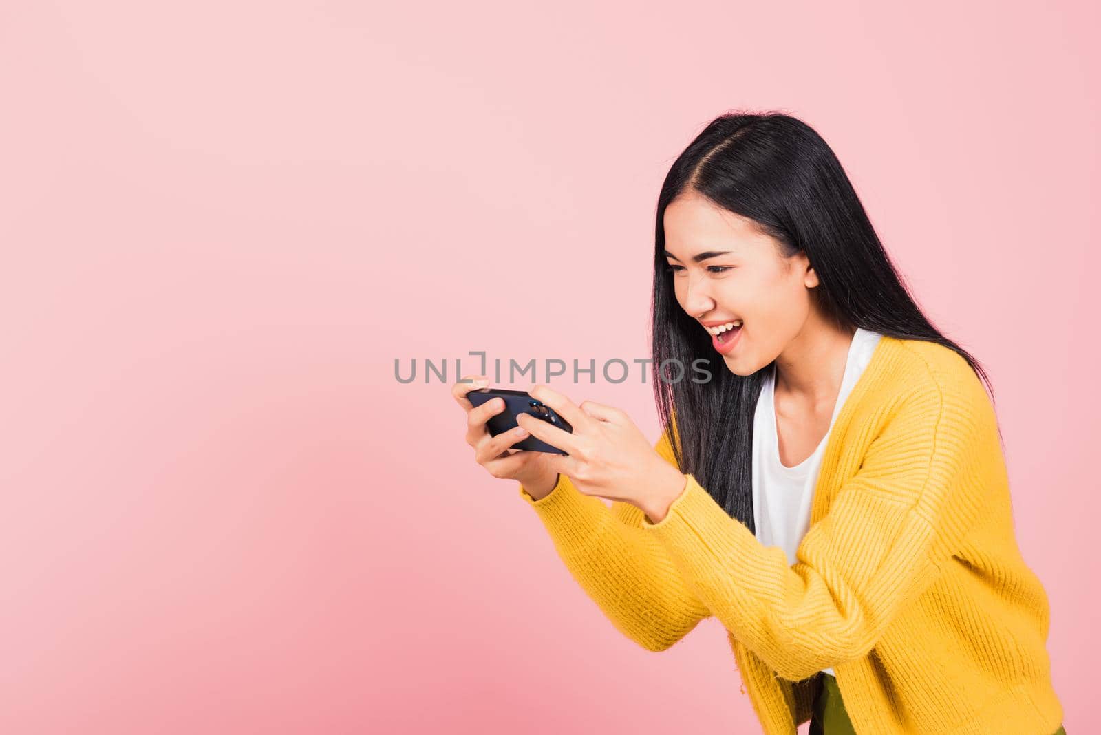 Happy Asian portrait beautiful cute young woman teen smiling excited   using mobile phone say yes! Studio shot isolated on pink background, Thai female surprised make winner gesture on smartphone