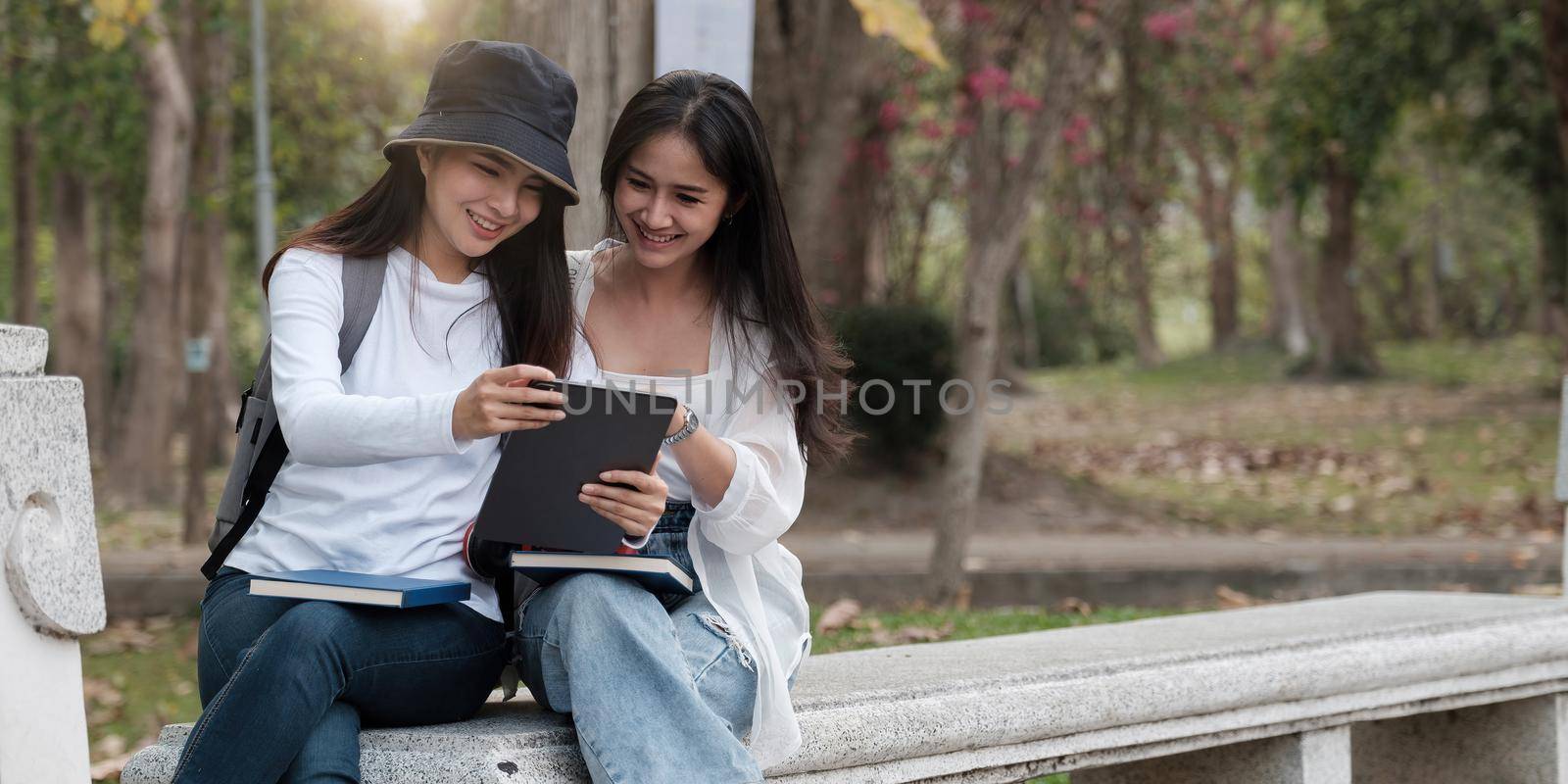 Two female university students outdoor study, using digital tablet together at the park in university