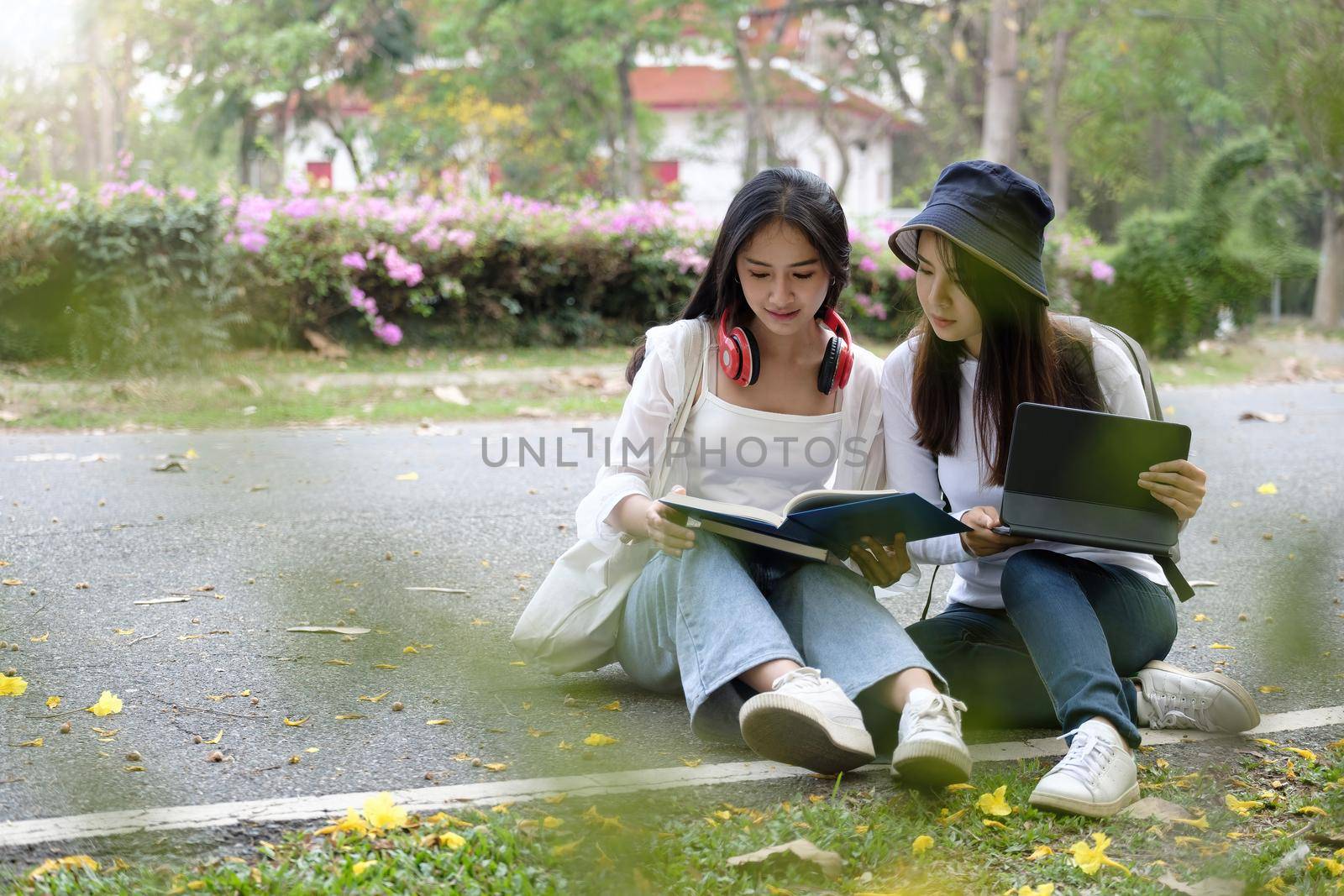 Two young pretty female university students outdoor study, tutoring to prepare for up coming their exam at park in university. by nateemee