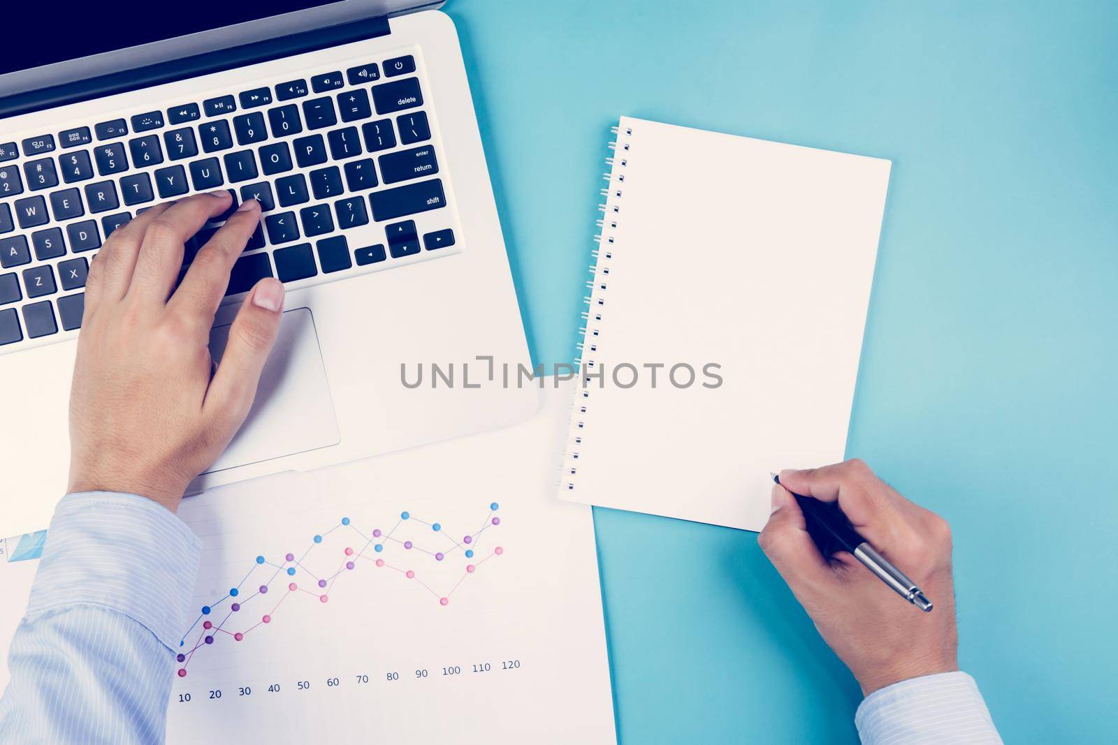 Hand of businessman looking documents report statistic financial with graph and chart and laptop computer and book on desk, finance and invest, digital marketing, business and communication concept.