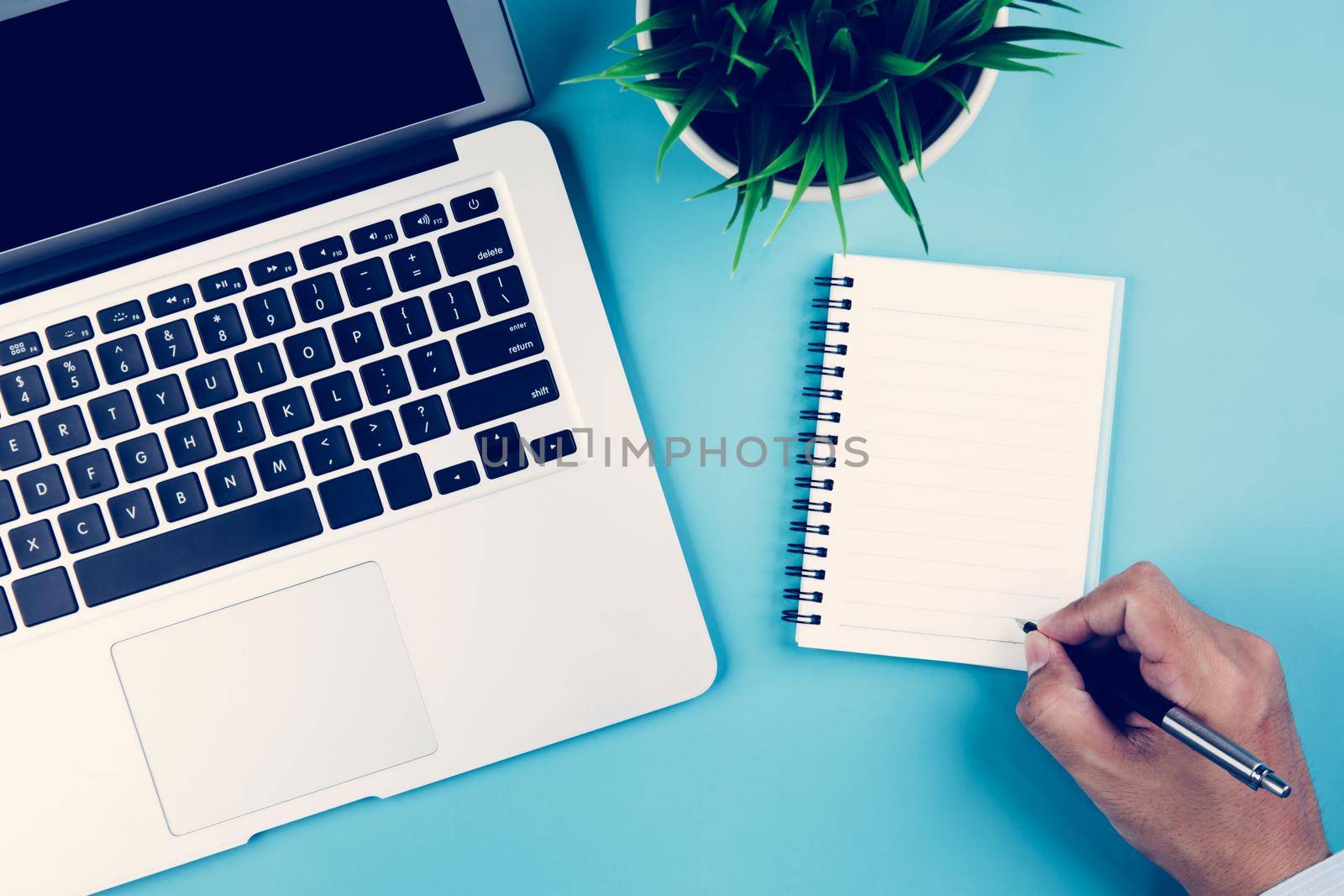 Flat lay, hand of businessman writing on notebook with Laptop computer and plant and pen on desk in office, workplace and notebook and potted tree and book, top view, business concept.