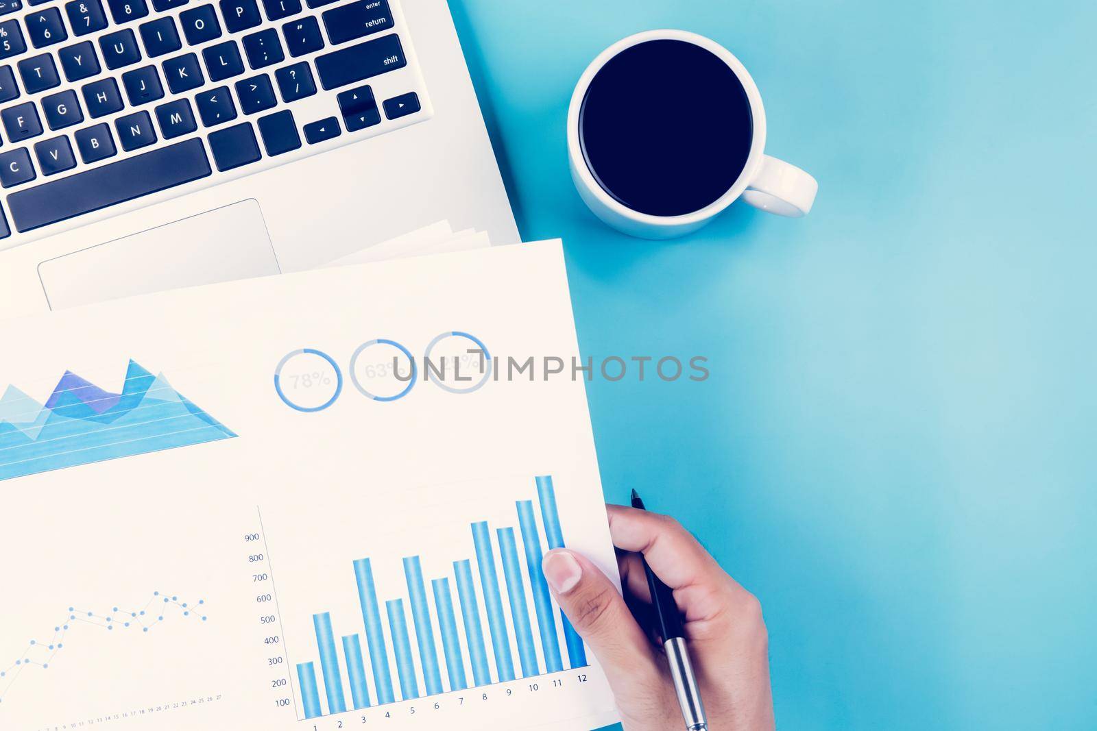 Hand of businessman holding documents report statistic financial with graph and chart and laptop computer and coffee on desk, finance and invest, digital marketing, business and communication concept. by nnudoo