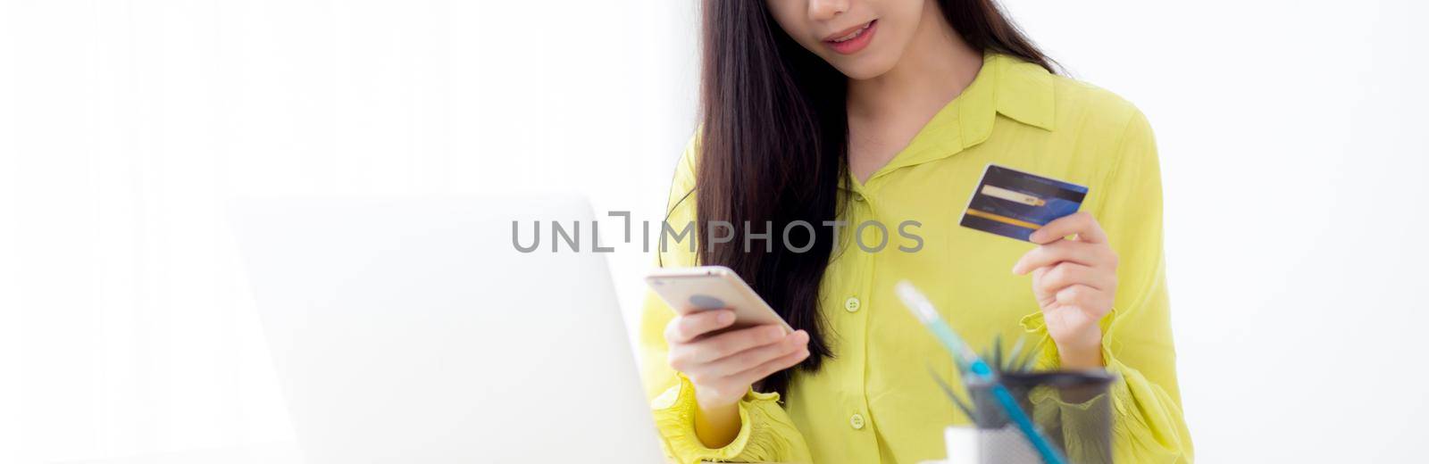 Young asian business woman using smart phone and holding credit card while online shopping and payment online with laptop computer on desk at home, female holding debit card, communication concept. by nnudoo